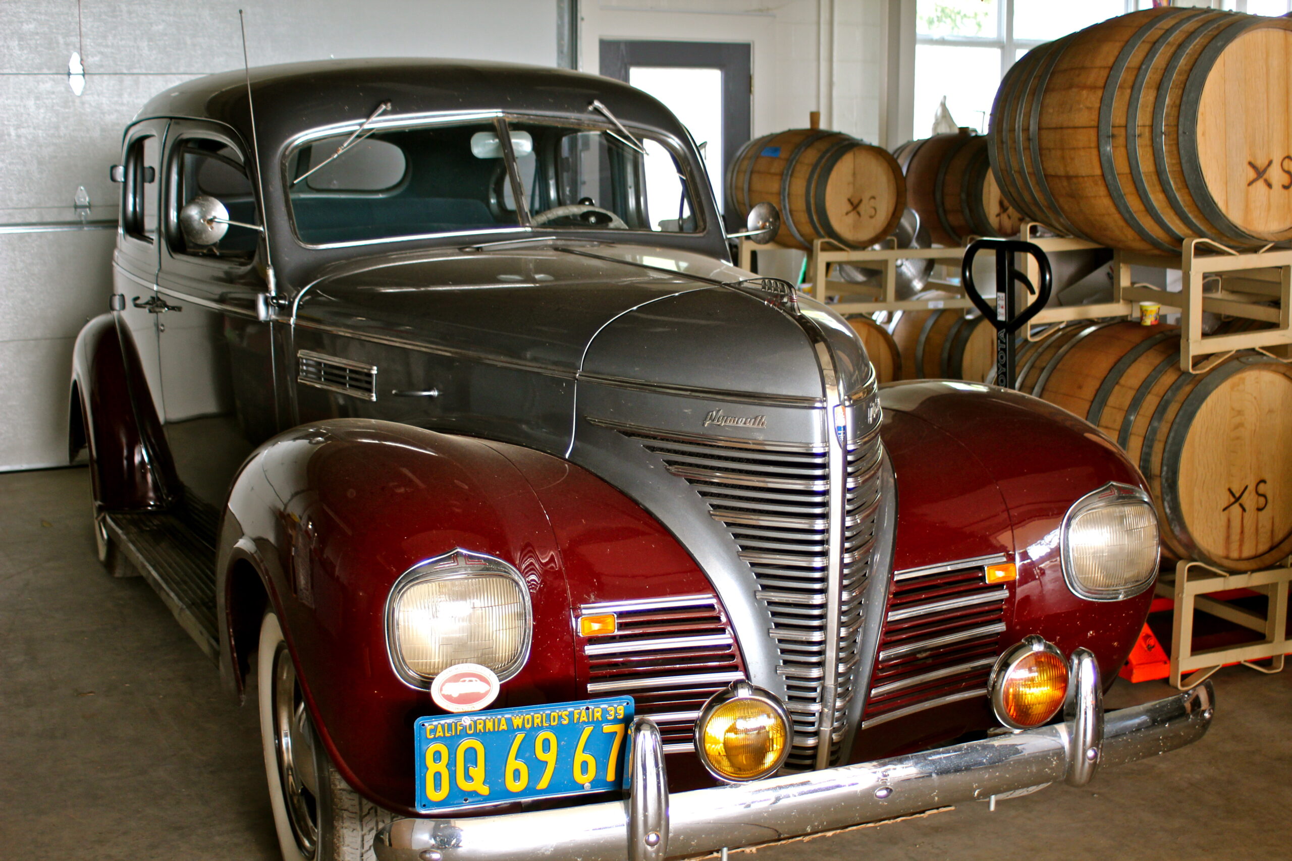 Classic vintage car parked inside a winery with wine barrels in the background.