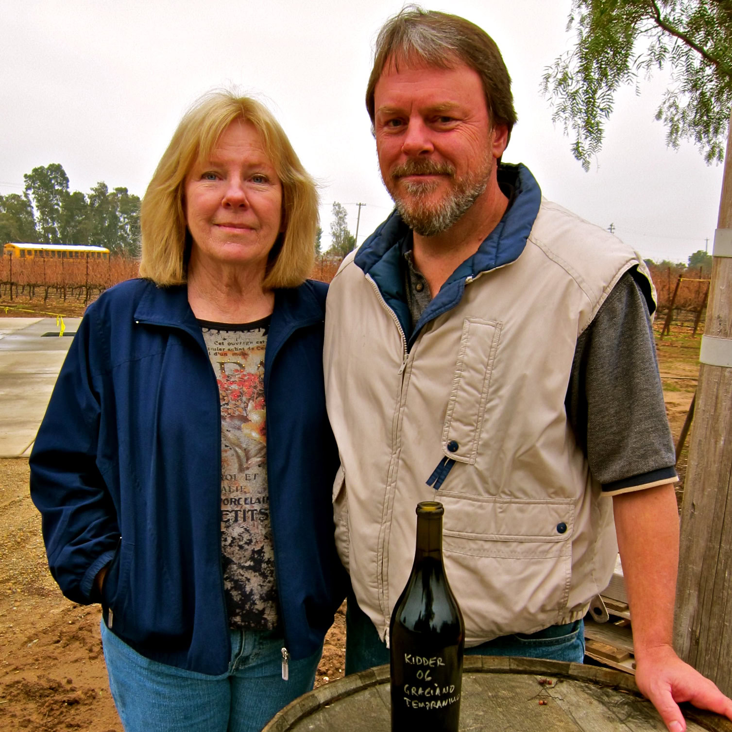 Two people at a vineyard with a wine bottle, representing Lodi Winegrape Commission activities.