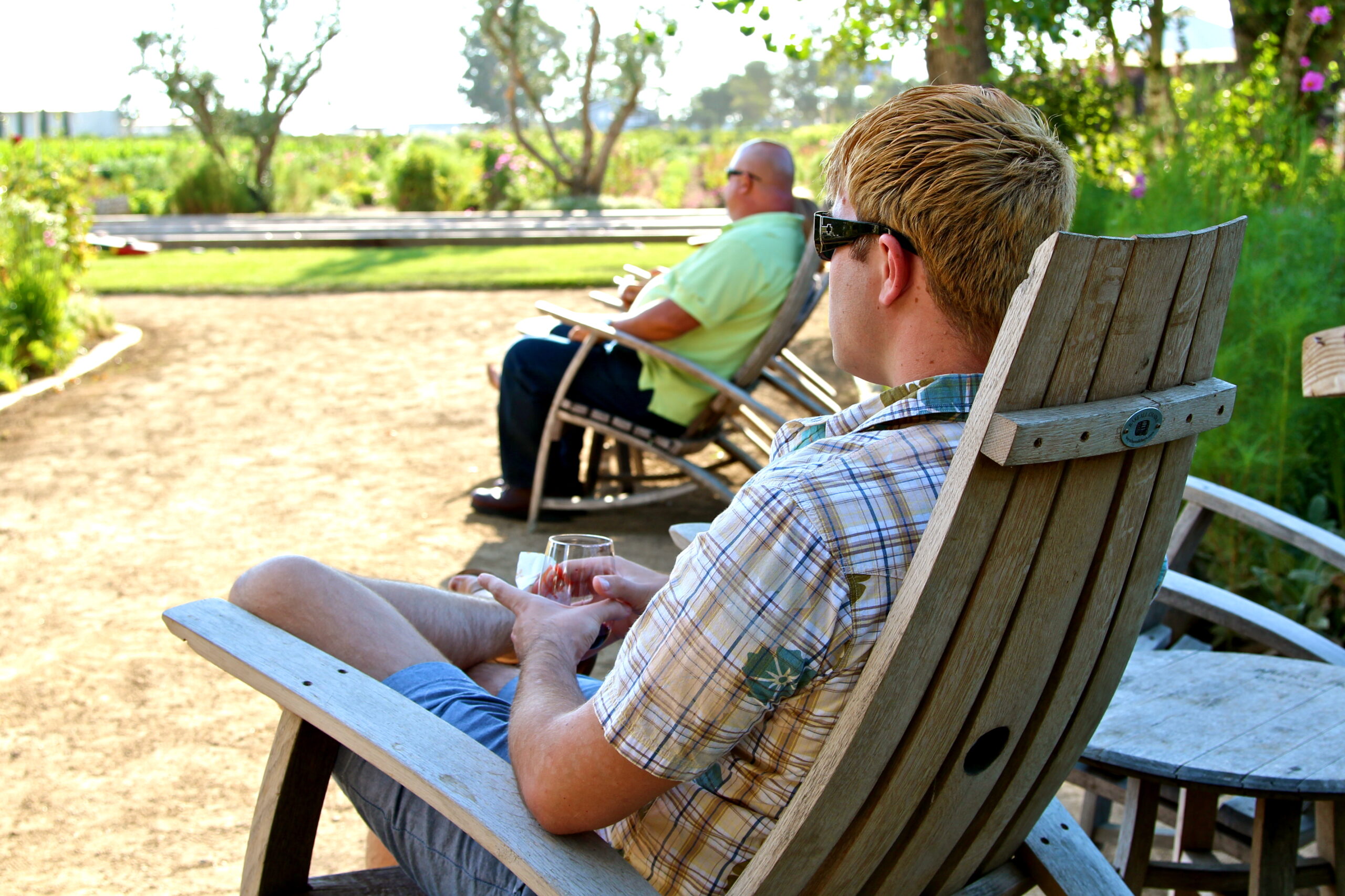 Two men relaxing outdoors in a vineyard, enjoying wine and sunshine, representing Lodi wine culture and winegrape production.