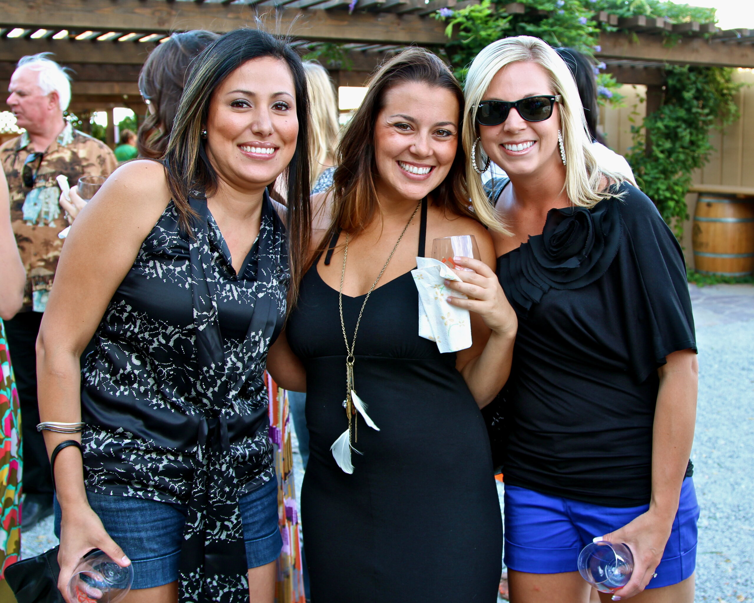 Three women smiling at a Lodi Winegrape Commission event, holding wine glasses outdoors.