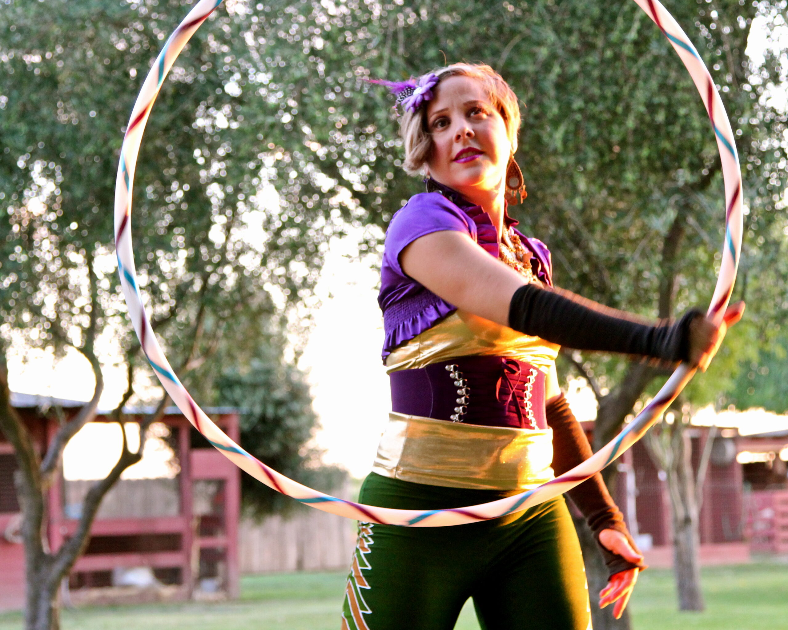 Circus performer spinning a hoop outdoors at a Lodi Wine event, with trees and a wooden fence in the background.