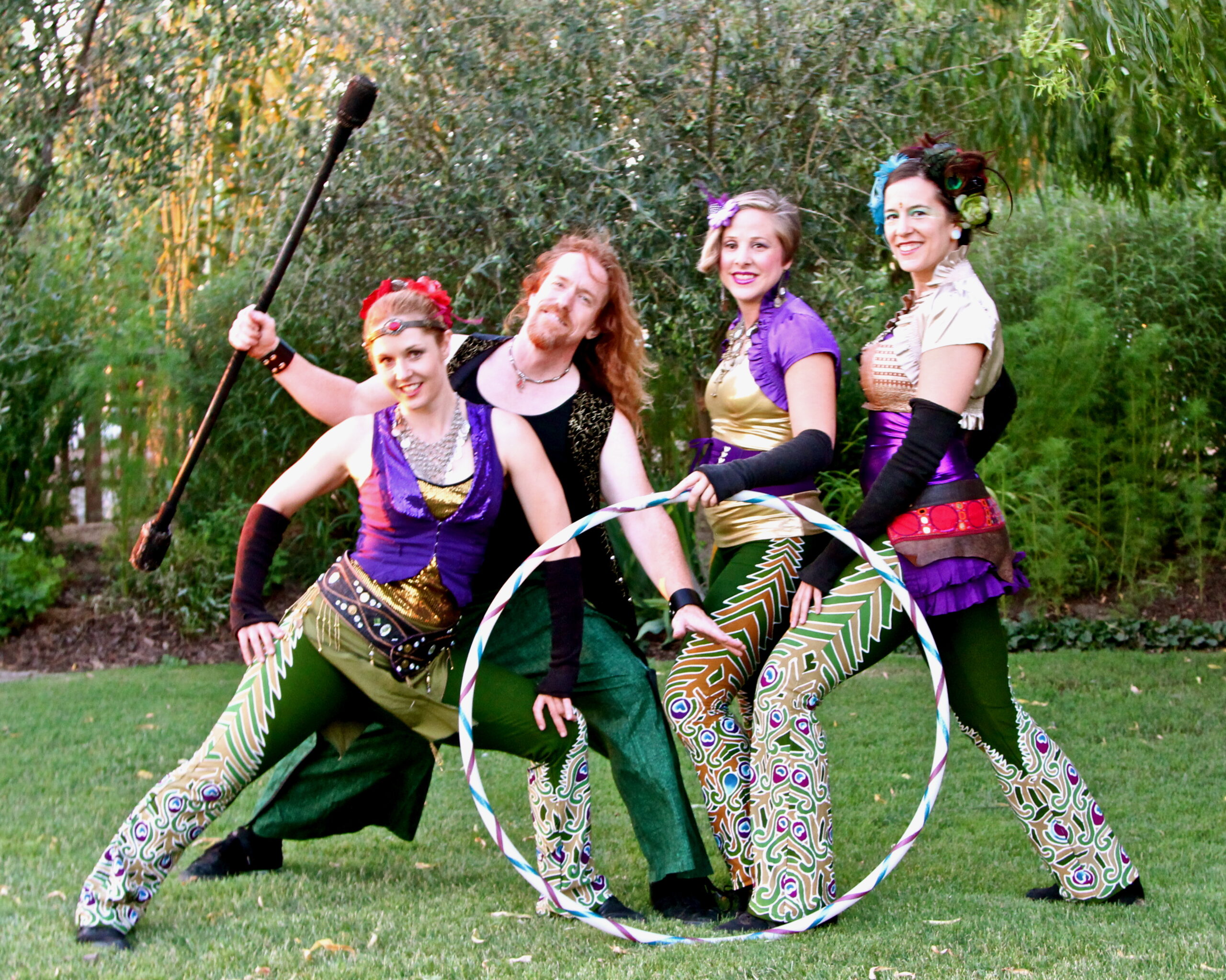 Group of four performers in colorful costumes with hula hoop and staff outdoors.