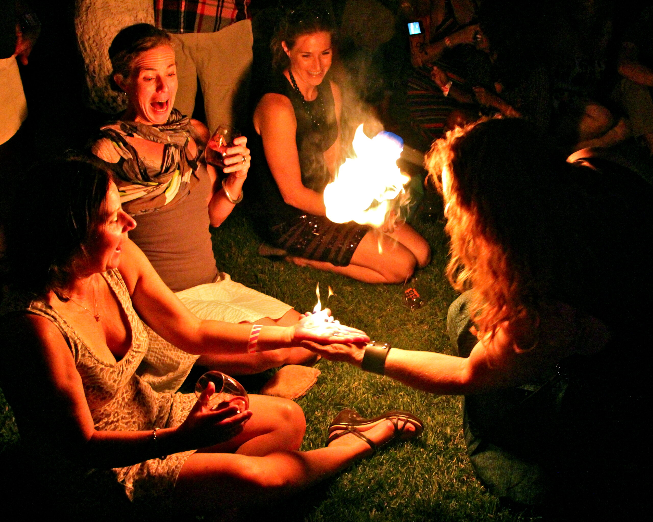 Group of women celebrating with a birthday cake and fire, enjoying a festive outdoor gathering at night.
