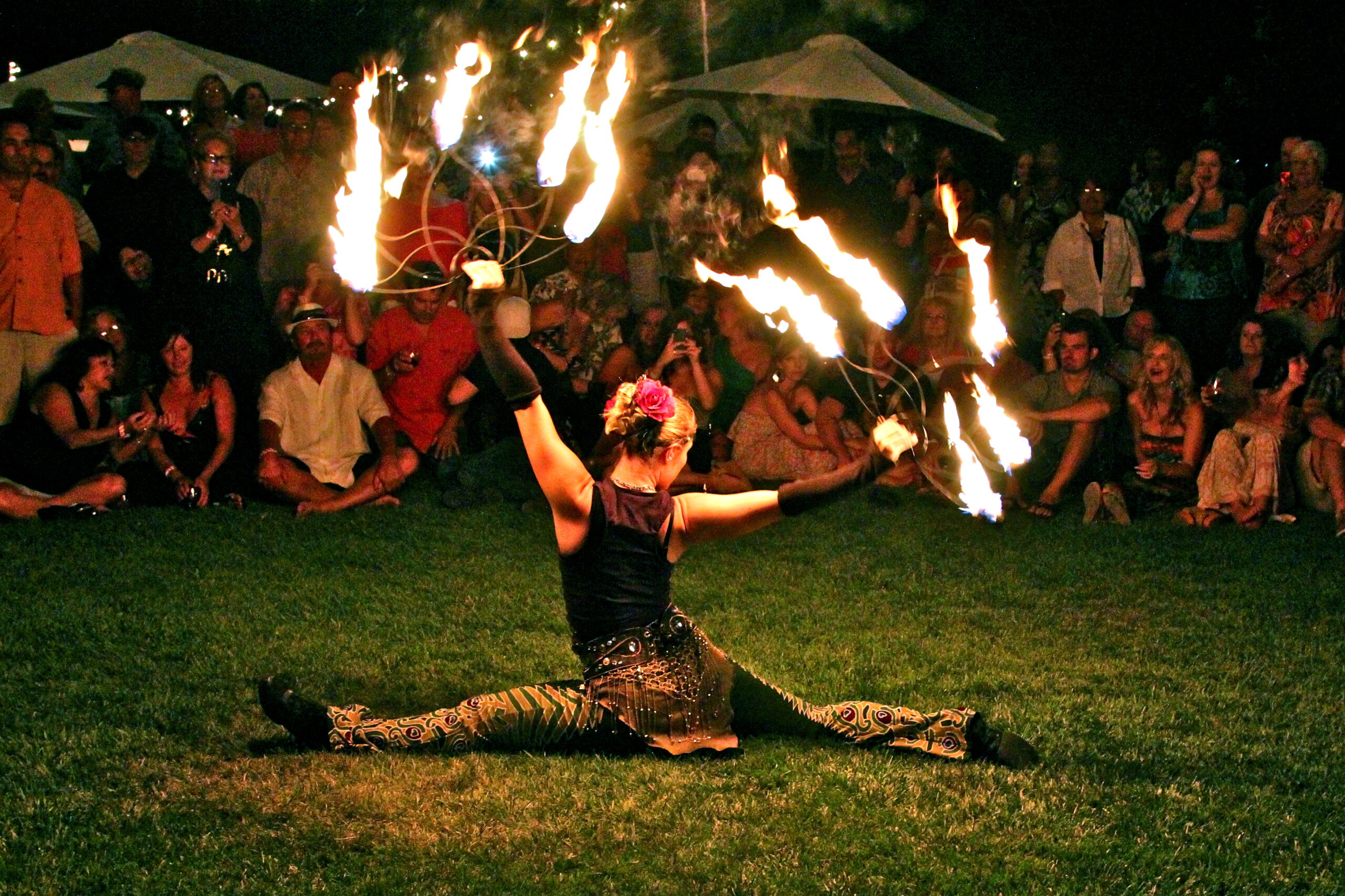 Performer doing fire dance at night with audience watching in the background.