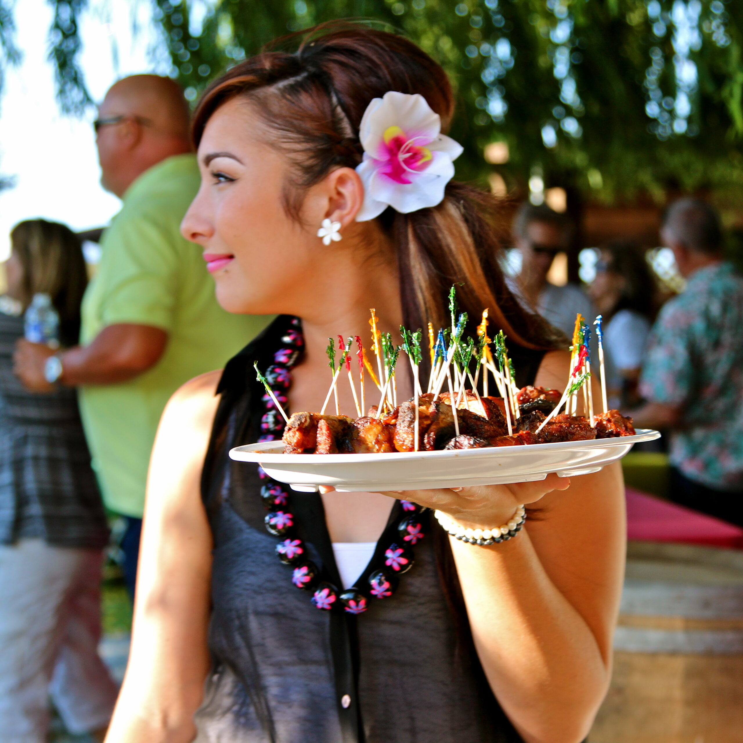 Woman holding a plate of appetizers at a Lodi wine event, with a flower in her hair and a lively outdoor setting.