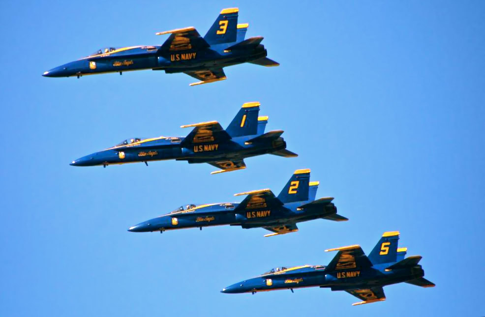 Five U.S. Navy Blue Angels fighter jets flying in tight formation against a clear blue sky.
