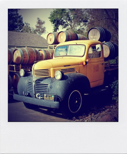 Old yellow truck carrying wine barrels, vintage style, outdoor setting, Lodi Winegrape Commission.