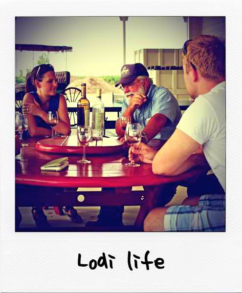 People enjoying wine tasting at Lodi Winegrape Commission event with wine bottles and glasses on table.