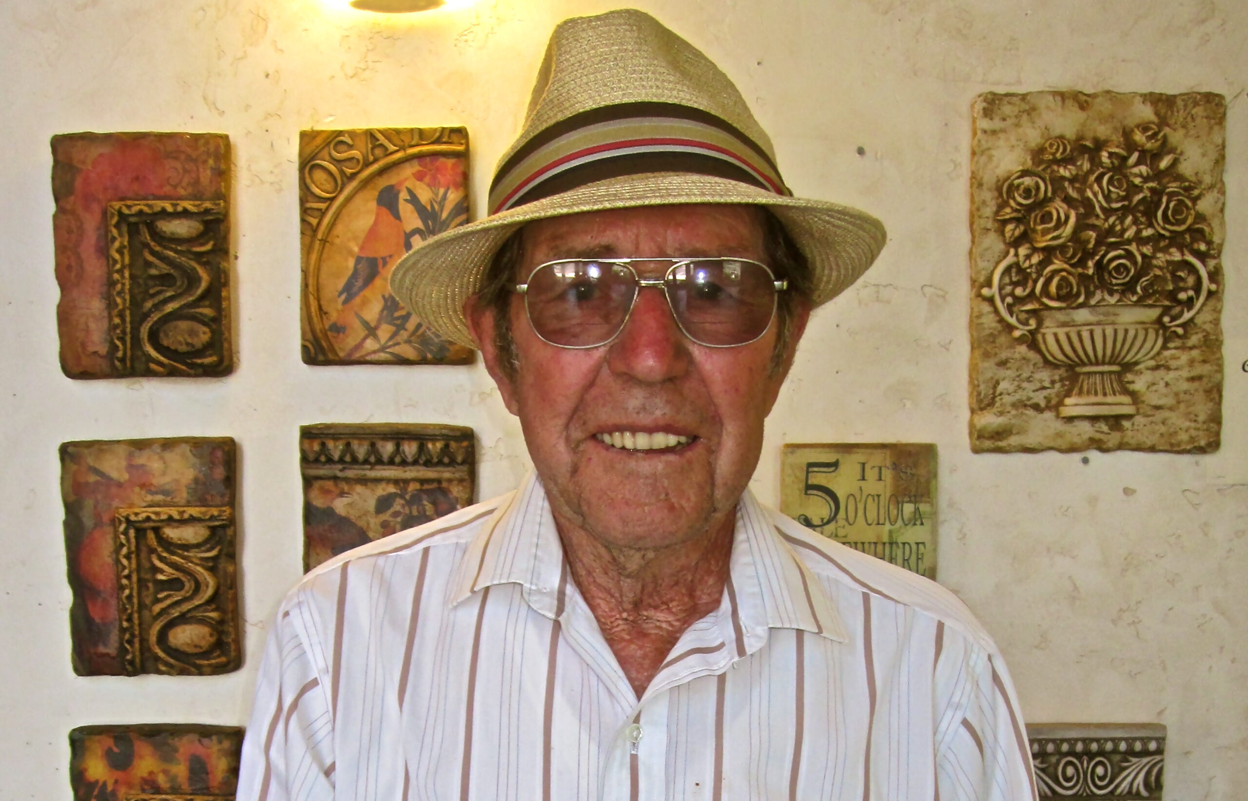 Elderly man wearing a hat and sunglasses at a Lodi wine event, with decorative art pieces in the background.