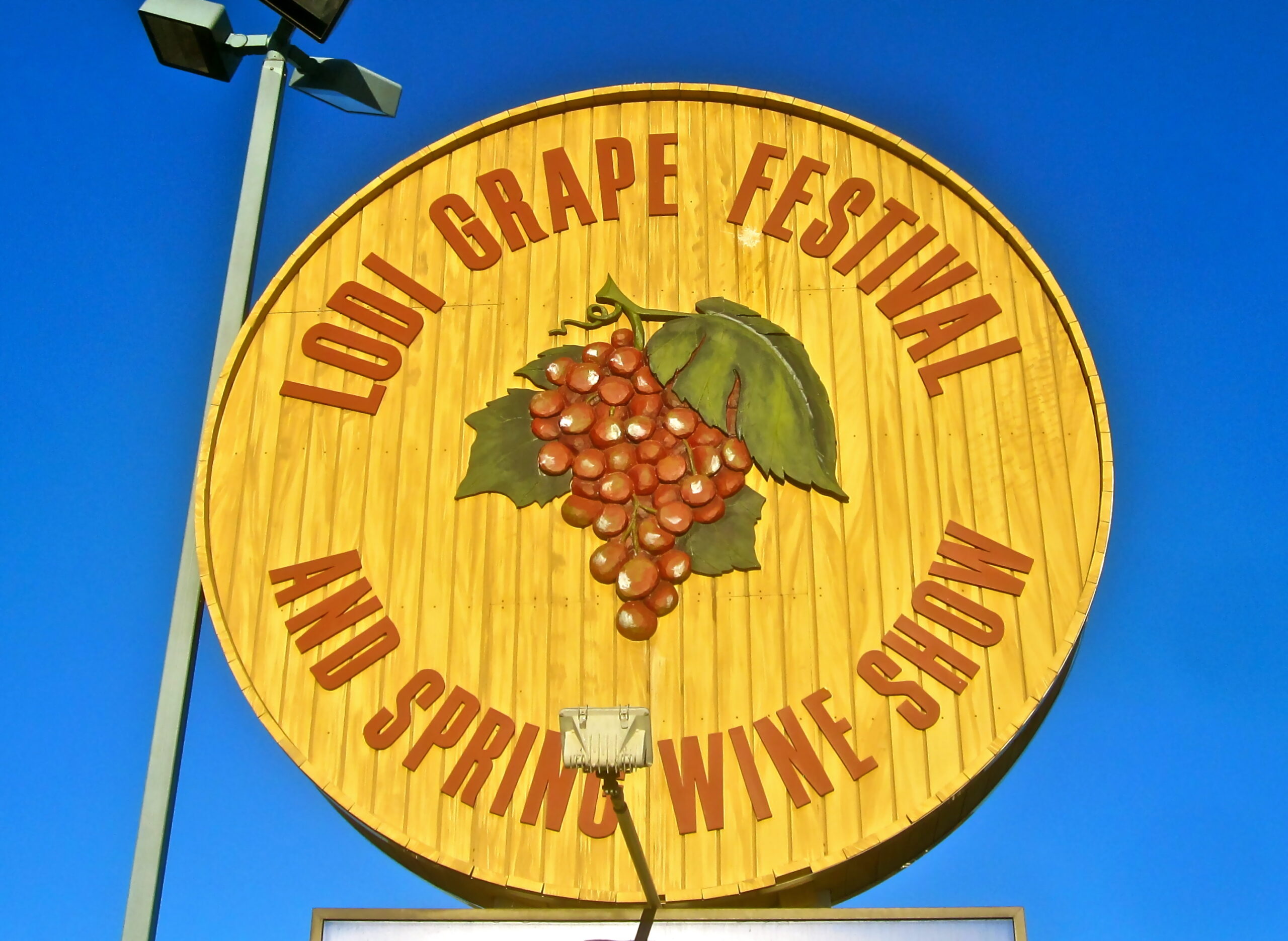 Large circular sign for Lodi Grape Festival and Spring Wine Show with grape cluster graphic against blue sky.