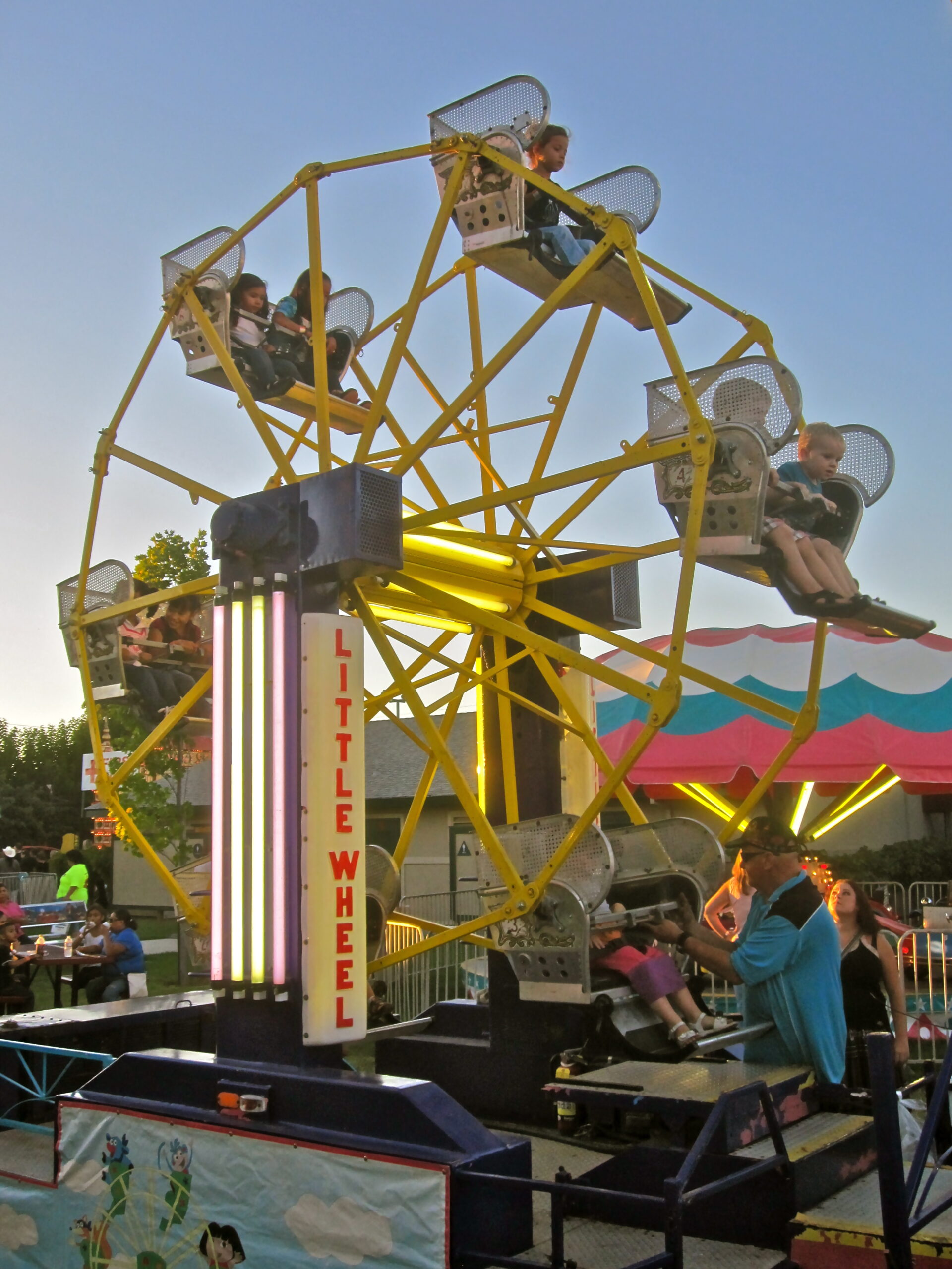 Colorful Ferris wheel at a fair with children enjoying rides and a clear sky in the background.