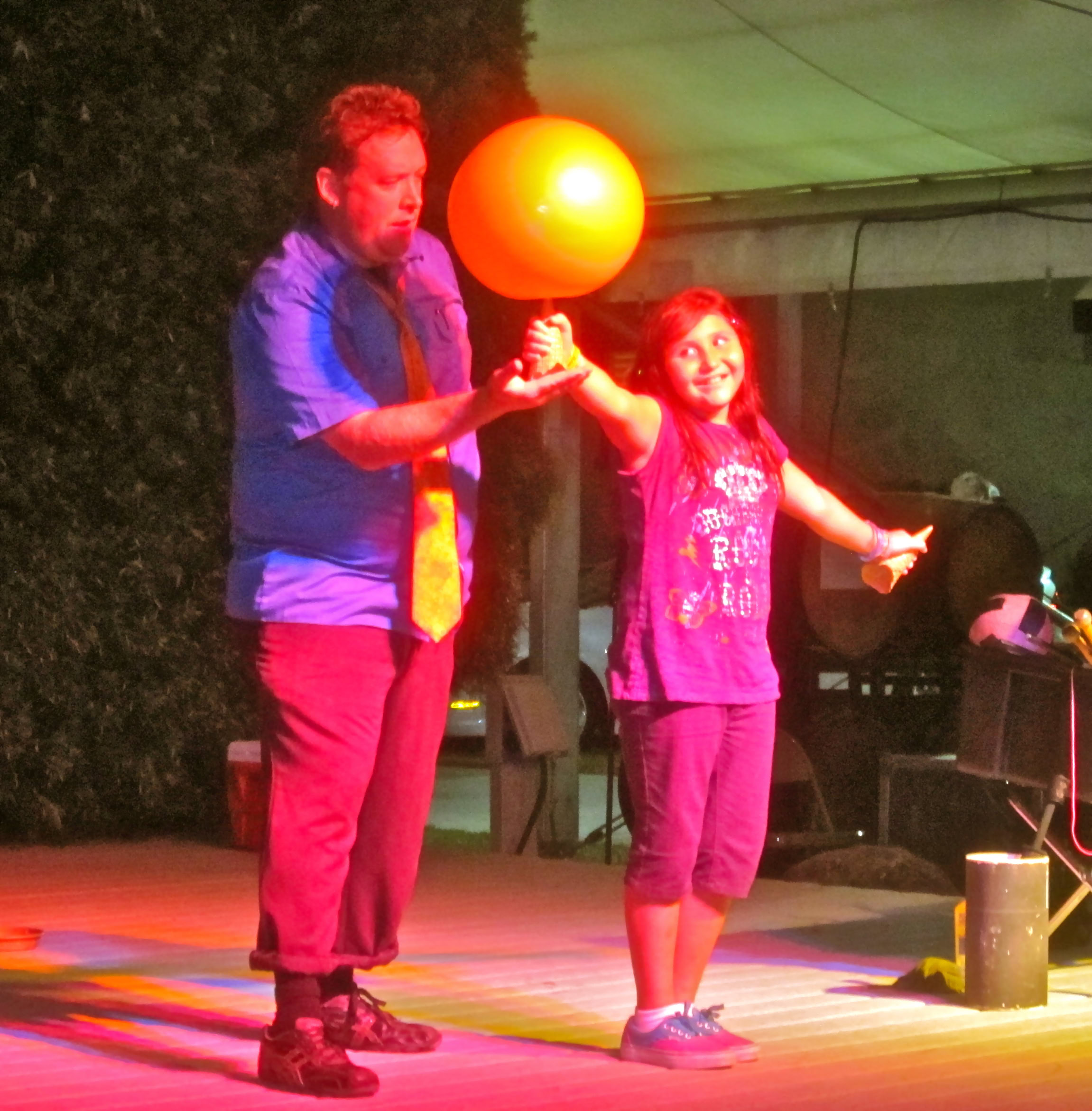 A man and a girl perform a magic trick with a glowing orange ball on stage at a Lodi Winegrape Commission event.