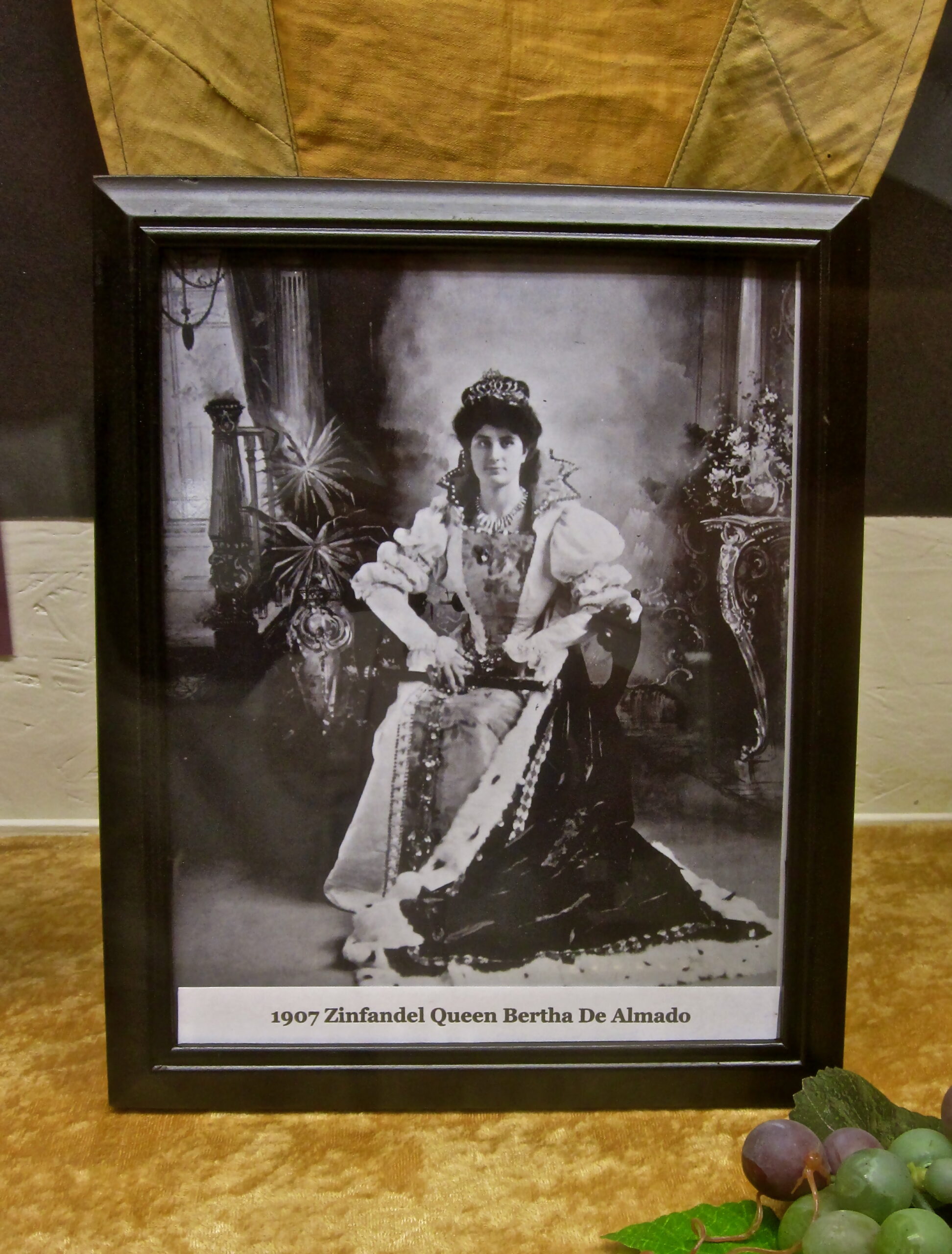 Black and white portrait of Queen Bertha De Almado in 1907, wearing a crown and elegant dress, seated with a scepter.