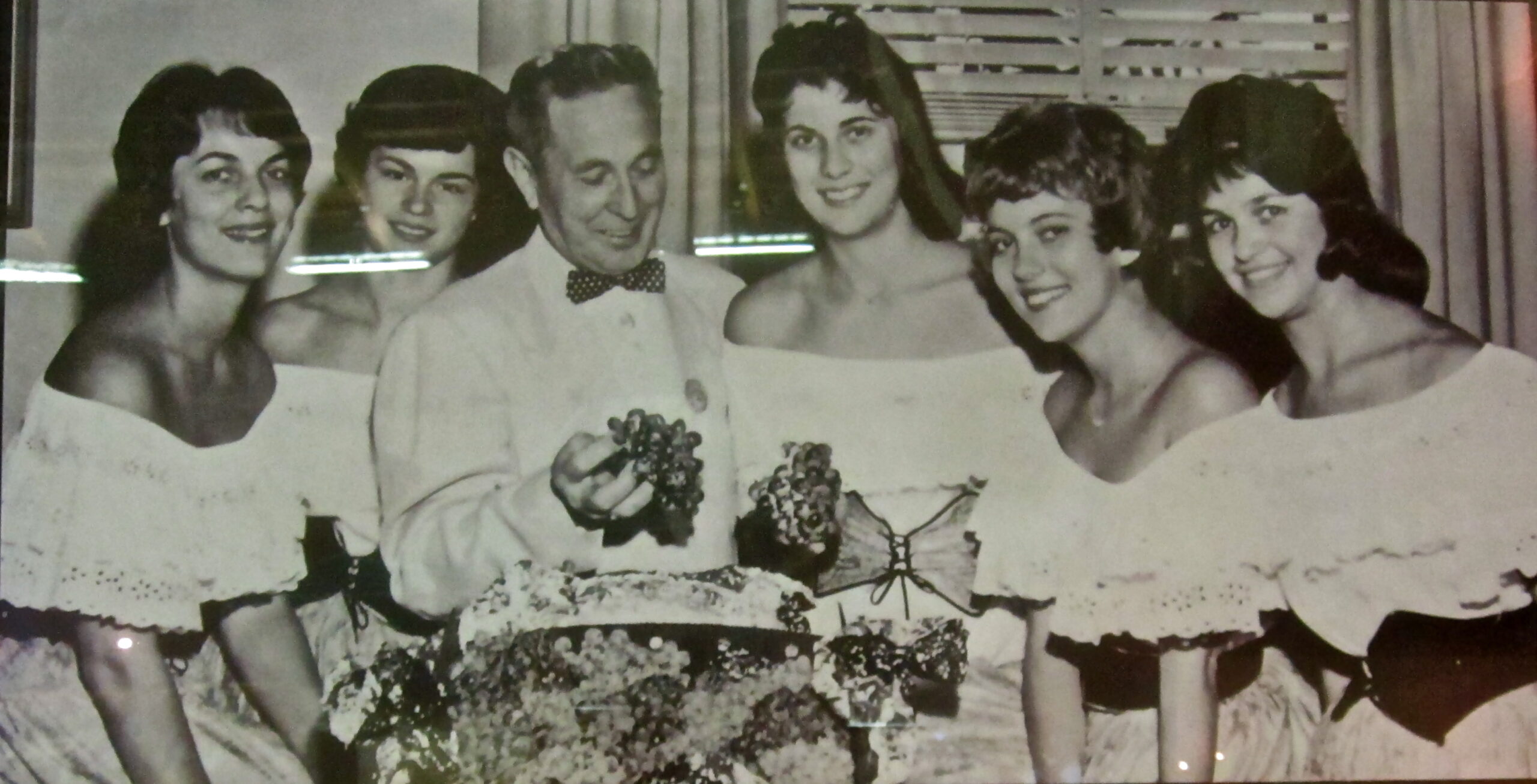 Group of women and man celebrating with cake, vintage black and white photo, nostalgic scene.