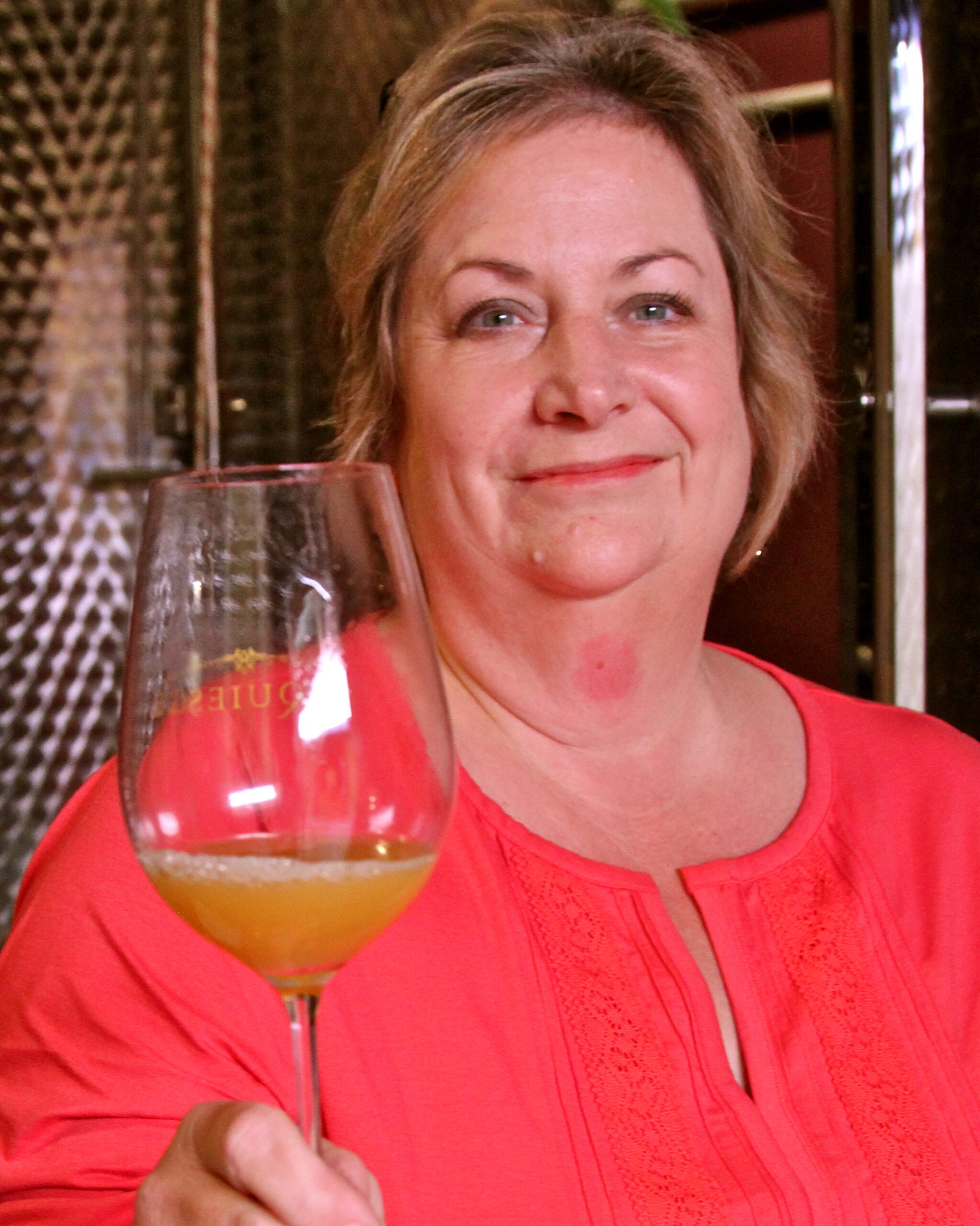 Woman holding a wine glass with a light-colored wine, smiling at a wine tasting event in Lodi, California.