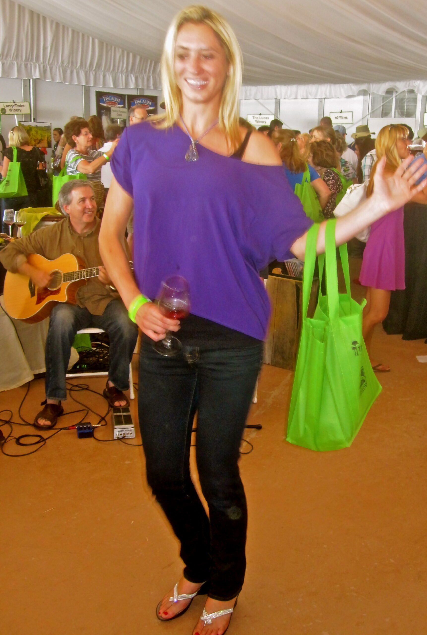 Woman holding a glass of wine at a wine event with a guitar player in the background.