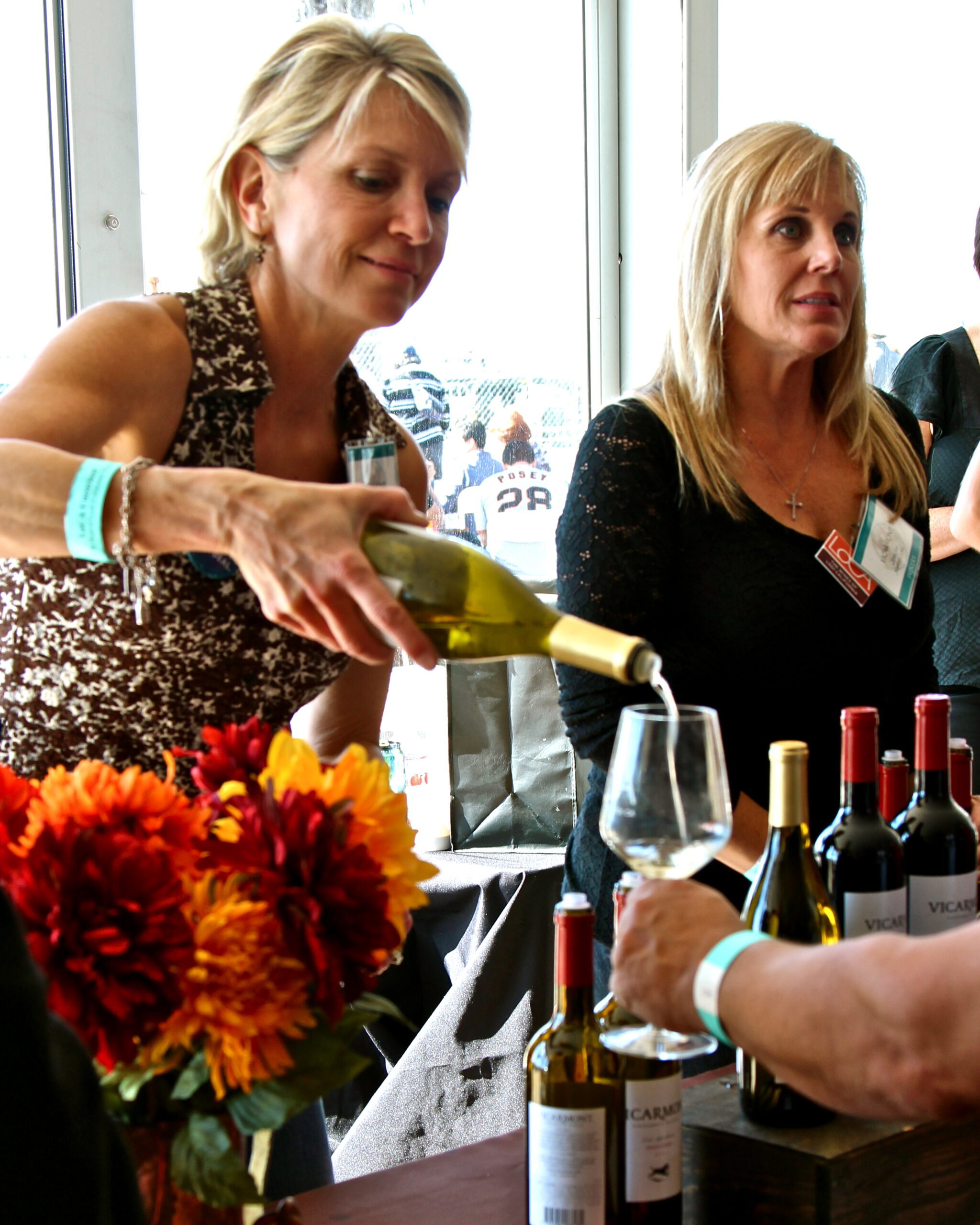 Women pouring wine at Lodi Winegrape Commission event with wine bottles and flowers.
