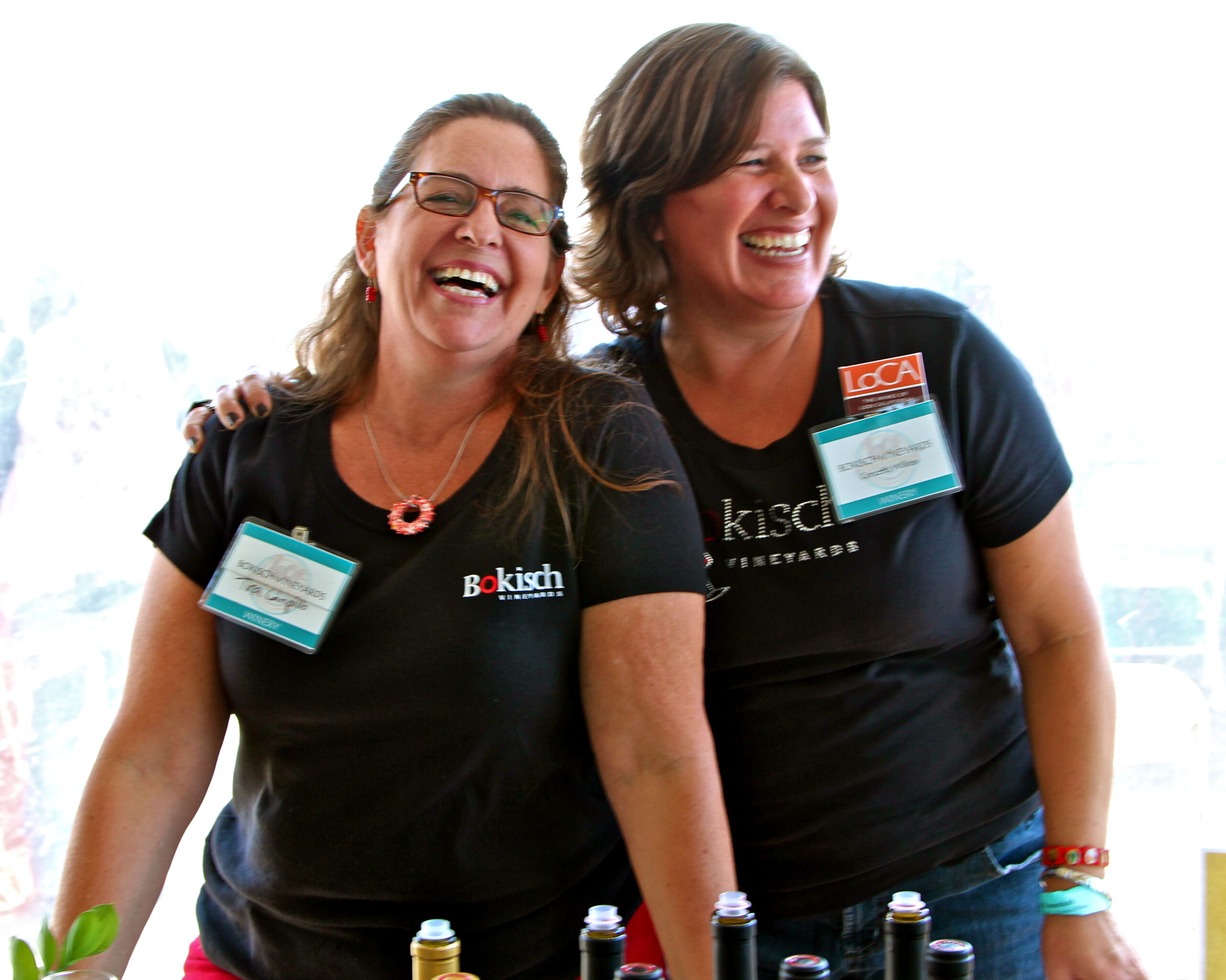 Two women smiling and laughing at a Lodi Winegrape Commission event, wearing black shirts with event badges.