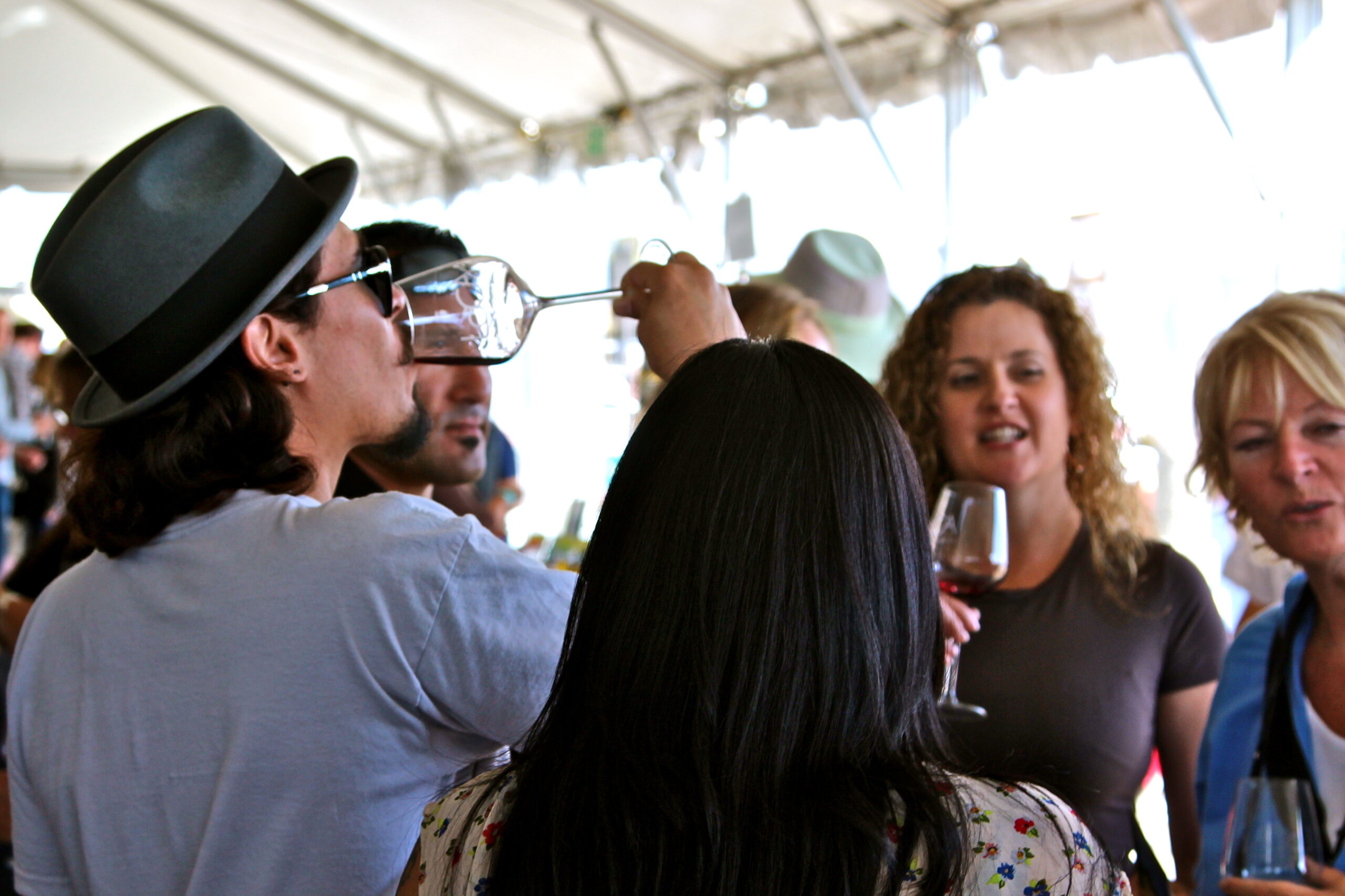 Group of people enjoying wine tasting at a Lodi Winegrape Commission event under a tent.