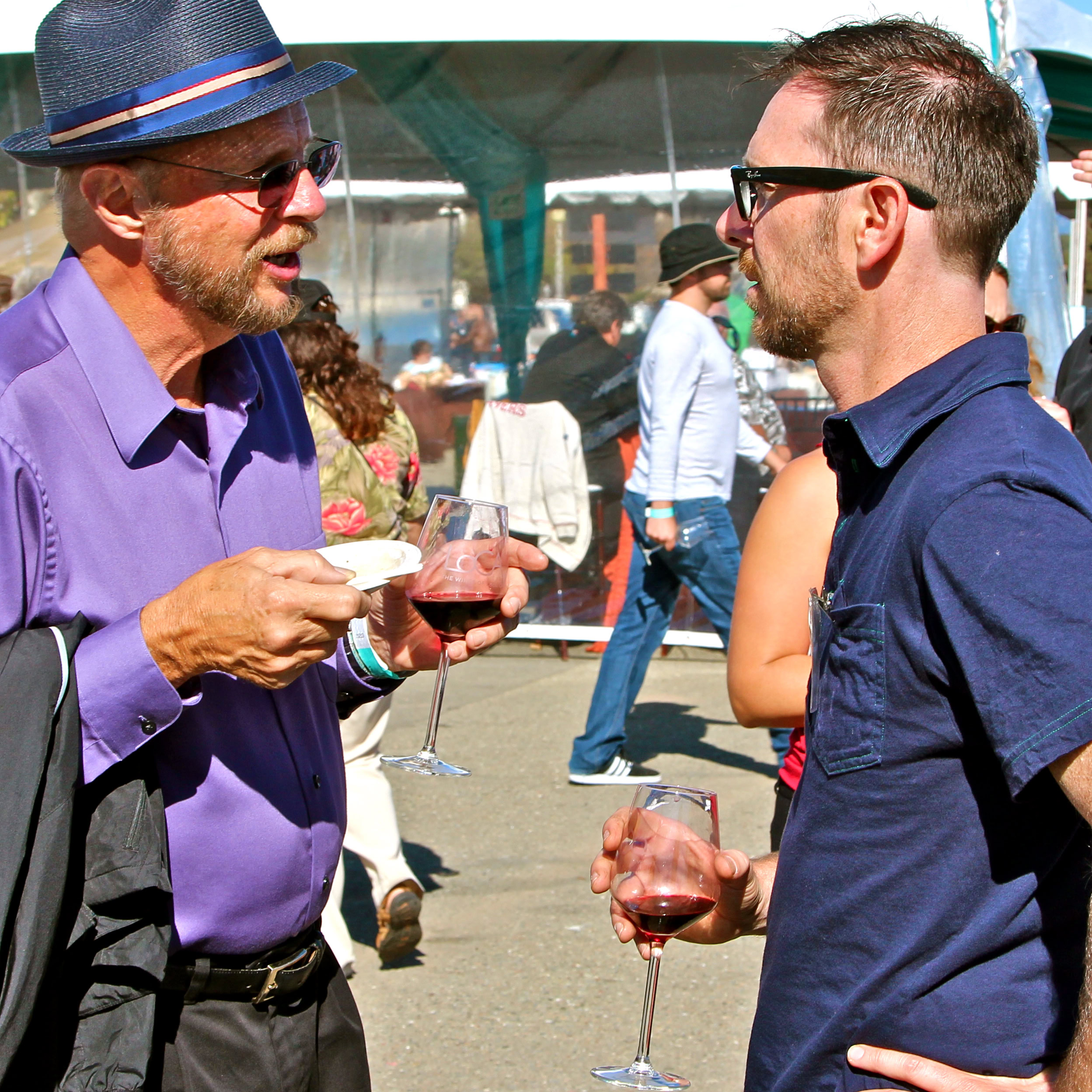 Two men enjoying wine at a Lodi Winegrape Commission event, engaging in conversation outdoors.