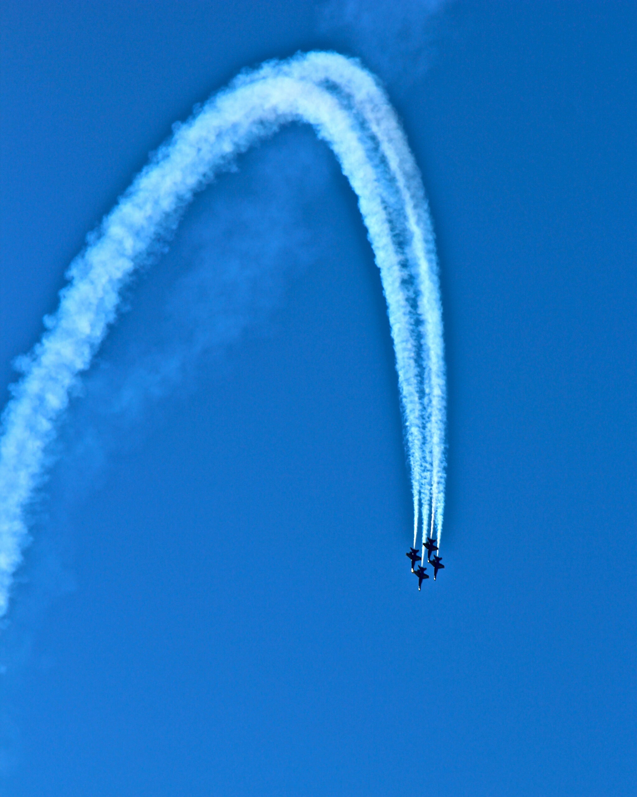 Two aircrafts perform an aerial stunt creating a smoke trail in a clear blue sky.
