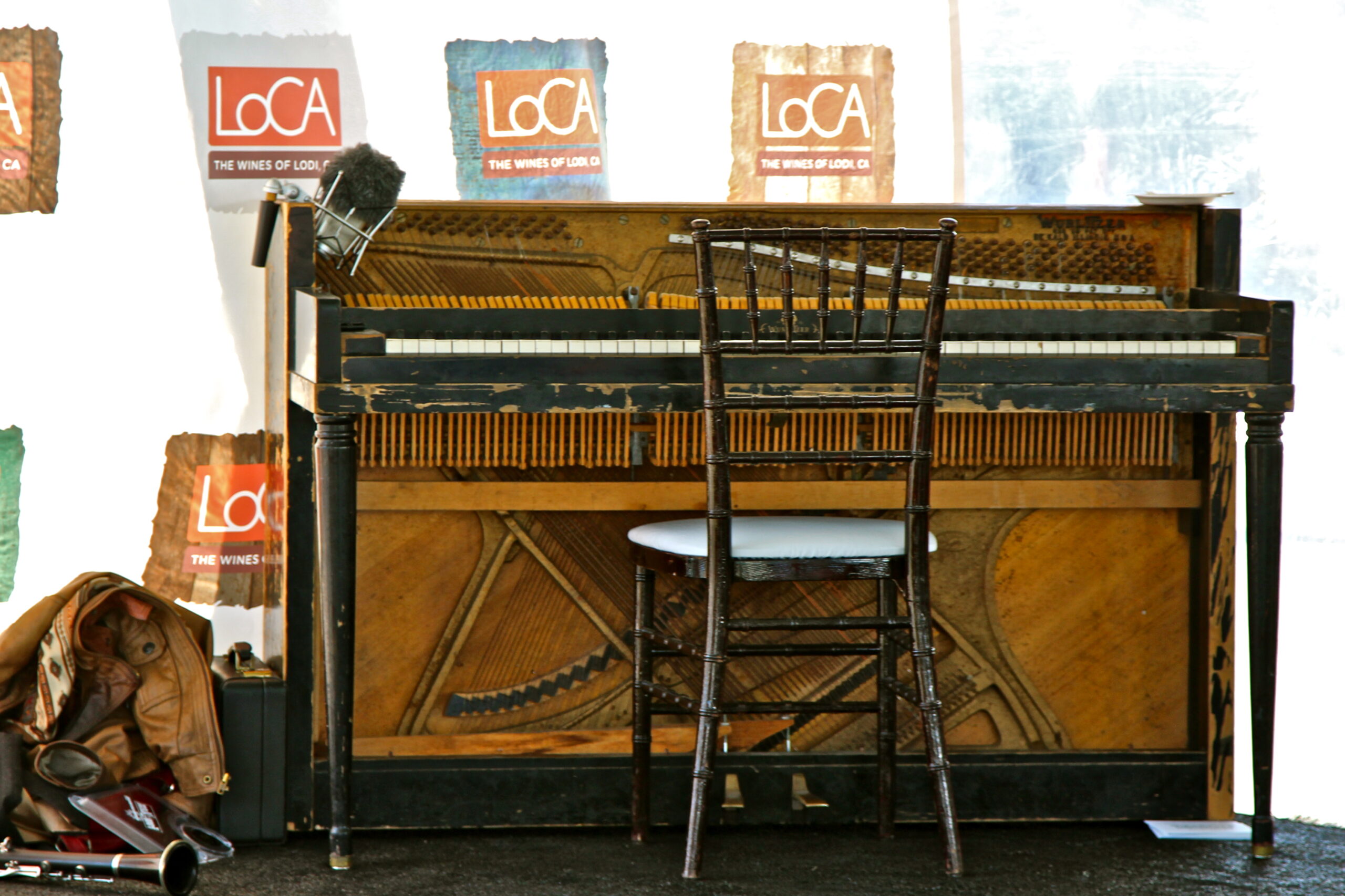 Vintage piano with a chair in front, Lodi Winegrape Commission banners in the background, at a wine event.