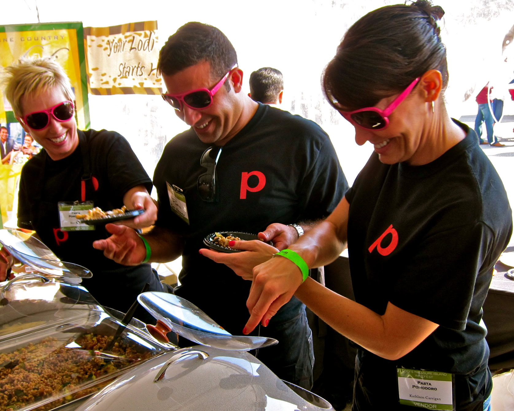 People enjoying food at Lodi Winegrape Commission event, wearing sunglasses and black shirts.