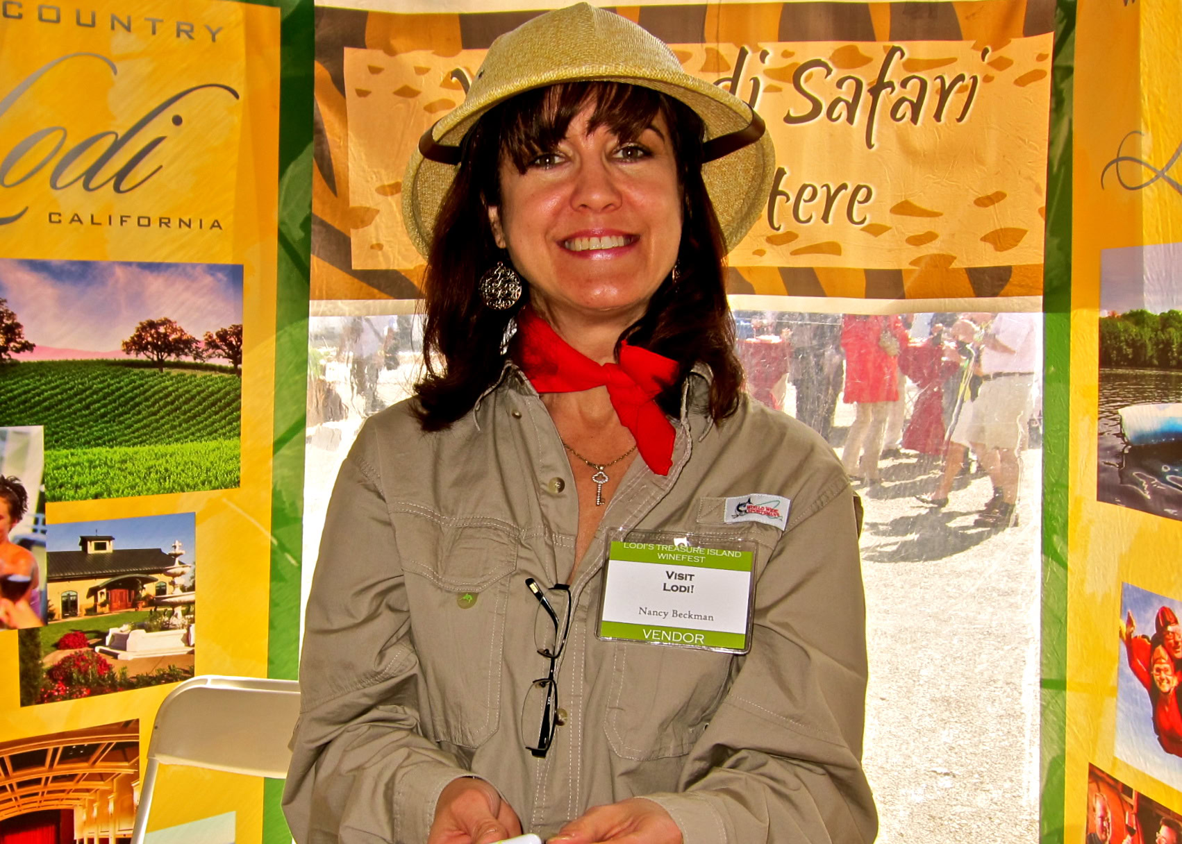 Woman at Lodi Winegrape Commission booth wearing a hat and red scarf, smiling at the event.