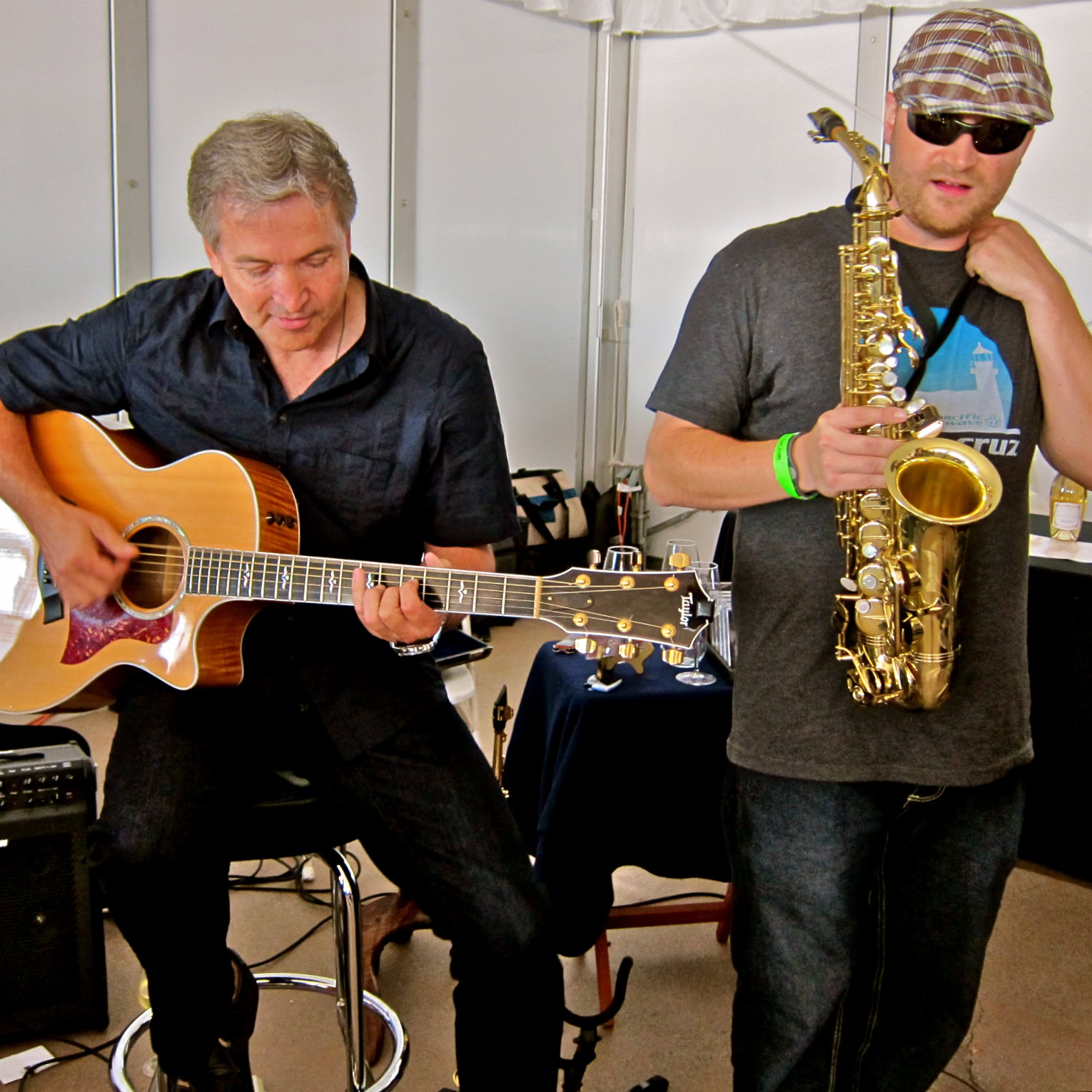 Musicians performing at a wine event, one playing guitar and the other with a saxophone, in a casual setting.