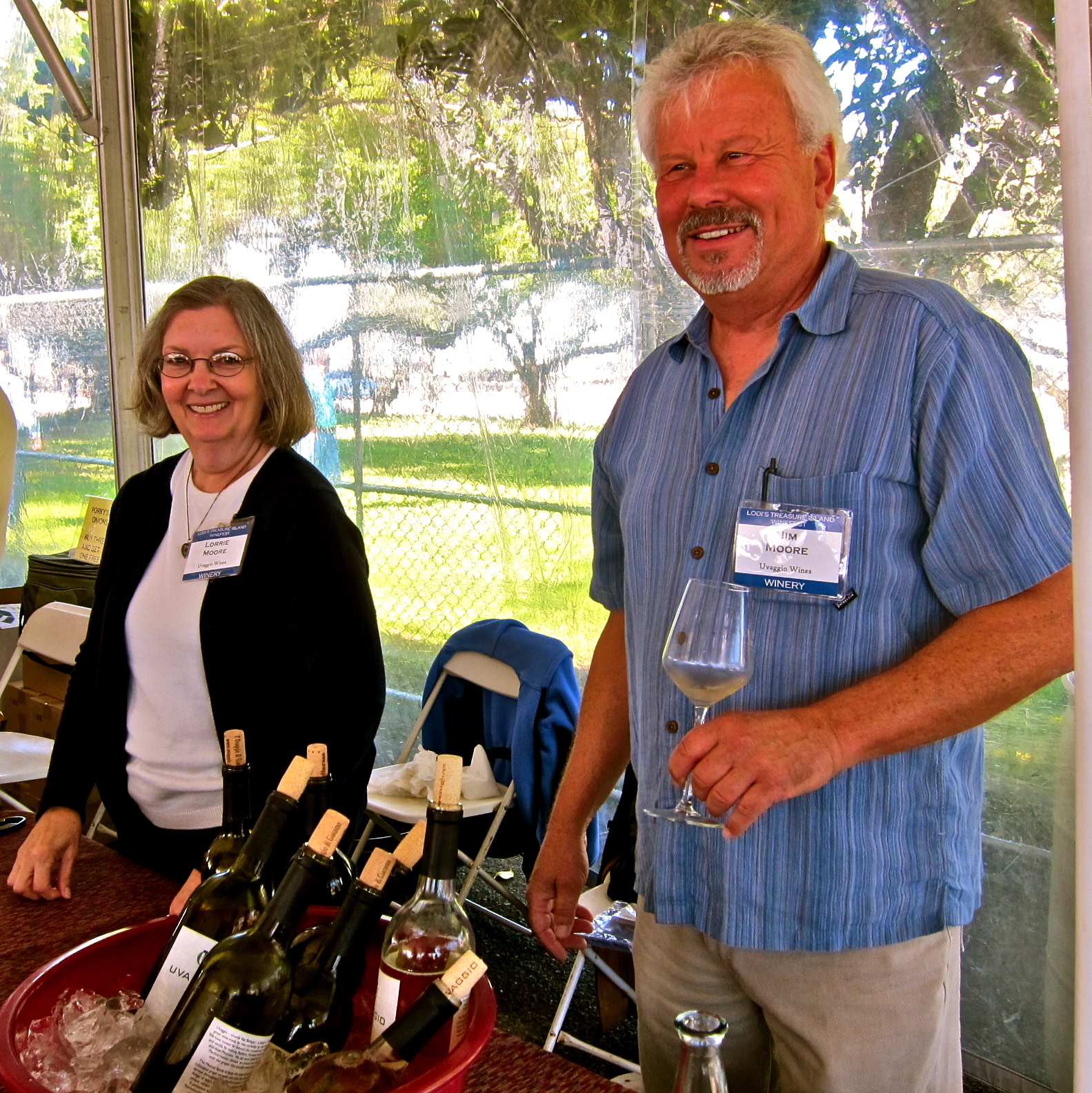 Smiling man holding a wine glass at a wine tasting event with bottles on display.