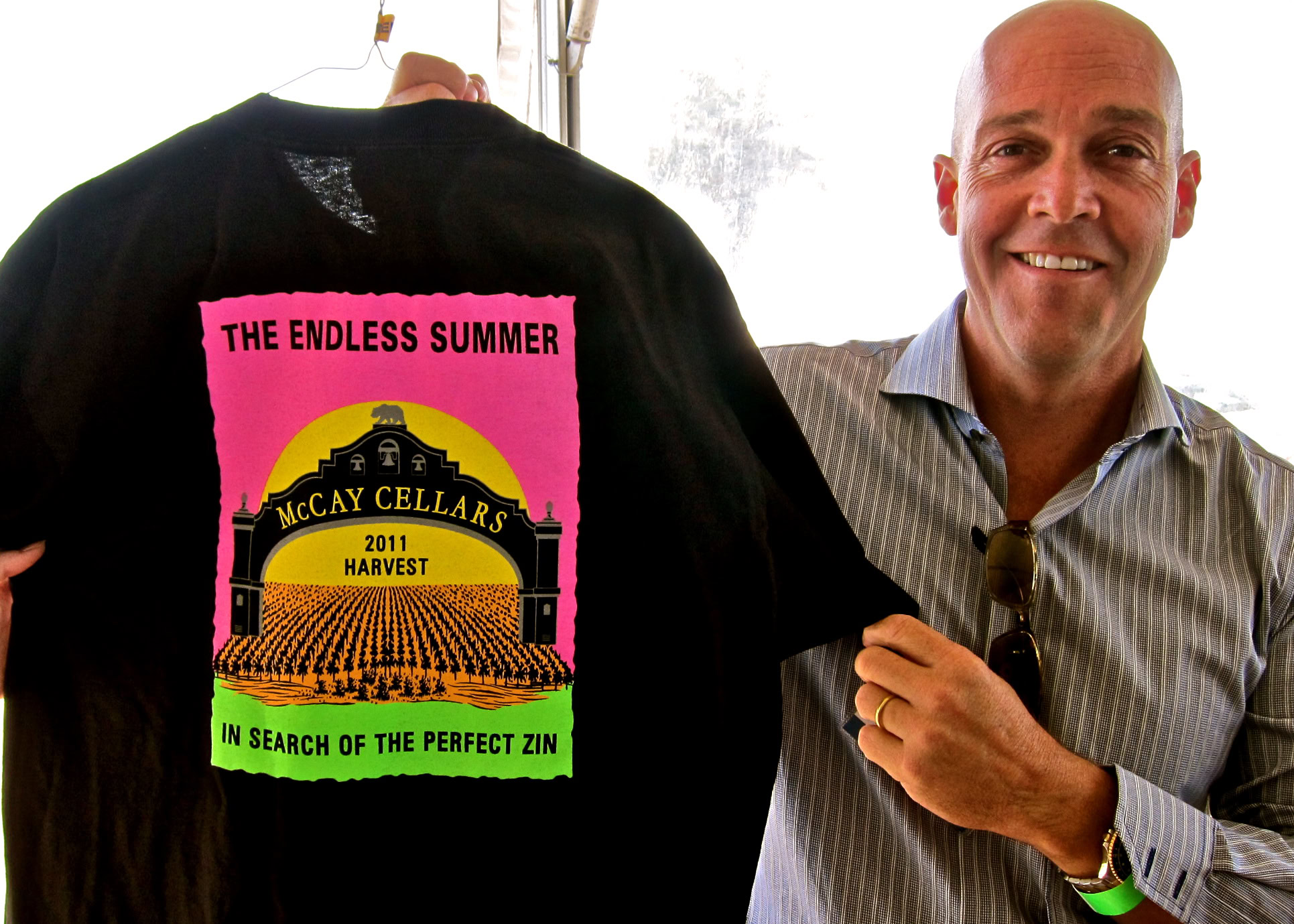 Man smiling at Lodi Winegrape Commission event holding a black T-shirt with colorful vineyard graphic.