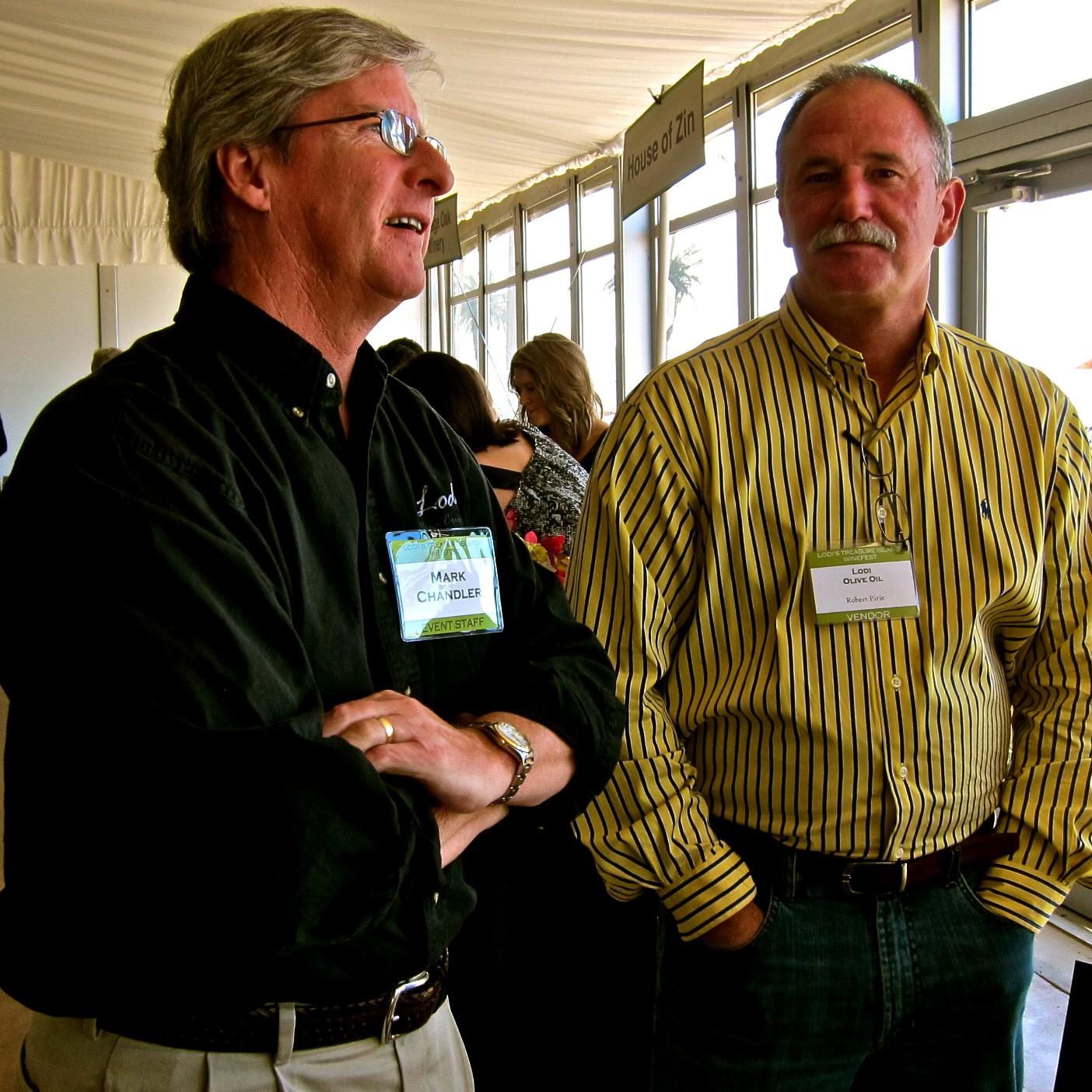 Two men at a wine event, engaging in conversation, with Lodi Winegrape Commission signage in the background.