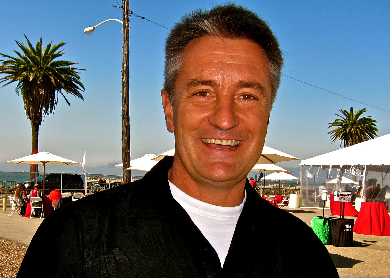 Smiling man at Lodi wine event with palm trees and outdoor tents in the background.