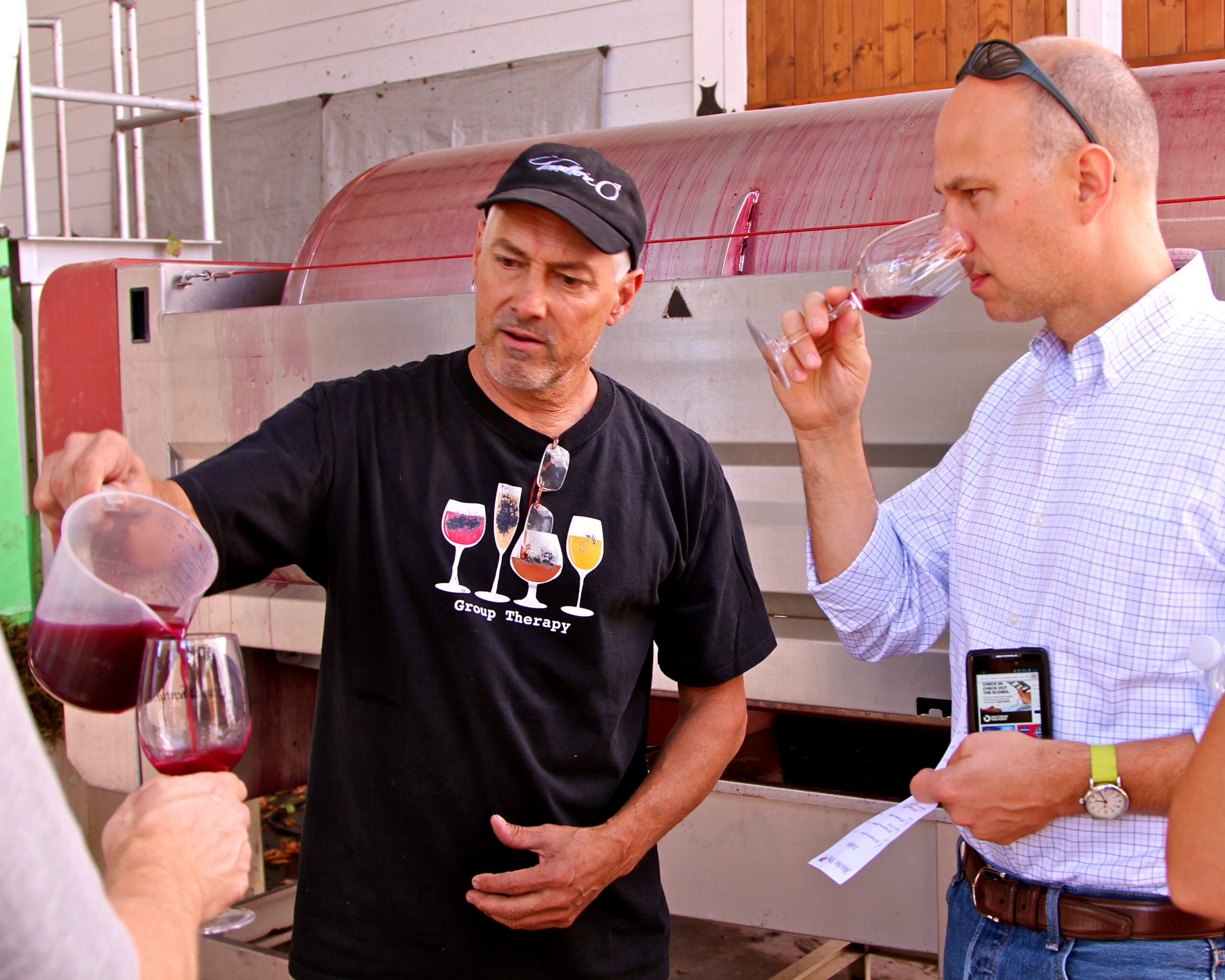 Two men tasting red wine at a Lodi wine event, one pouring and the other smelling the wine.