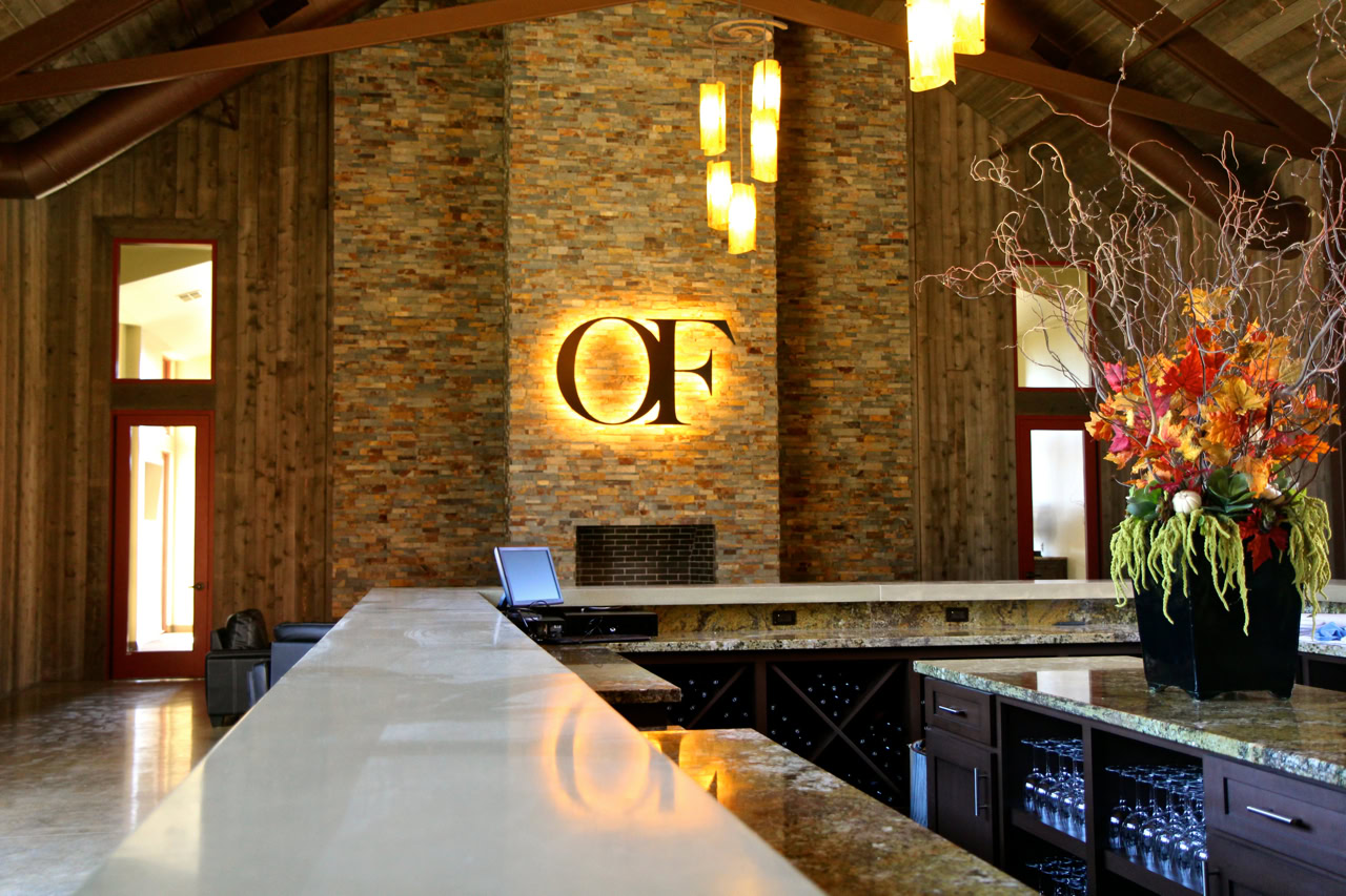 Modern winery office interior with stone wall, illuminated OF sign, and floral arrangement at the bar.