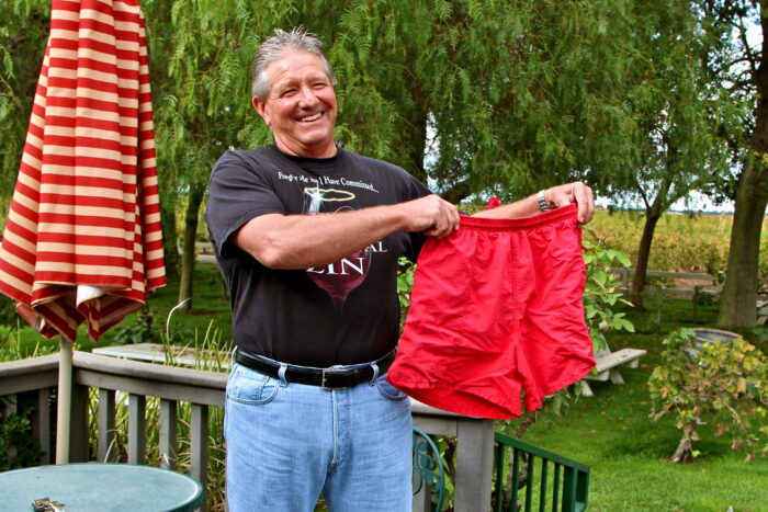 Smiling man holding red shorts outdoors at Lodi Winegrape Commission event.