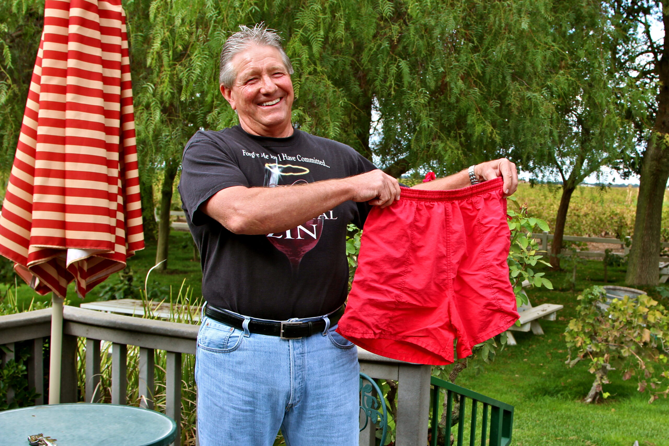 Smiling man holding red shorts outdoors at Lodi Winegrape Commission event.