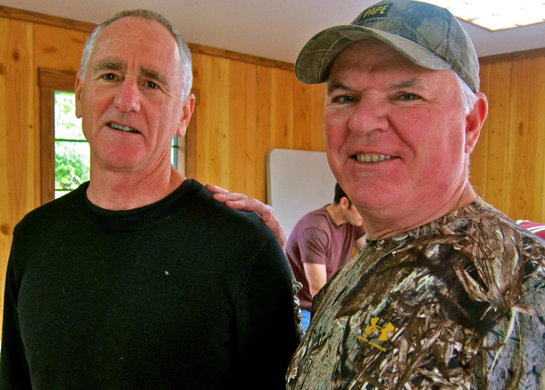Two men smiling indoors, one in a black shirt and the other in camouflage, at a Lodi Winegrape Commission event.