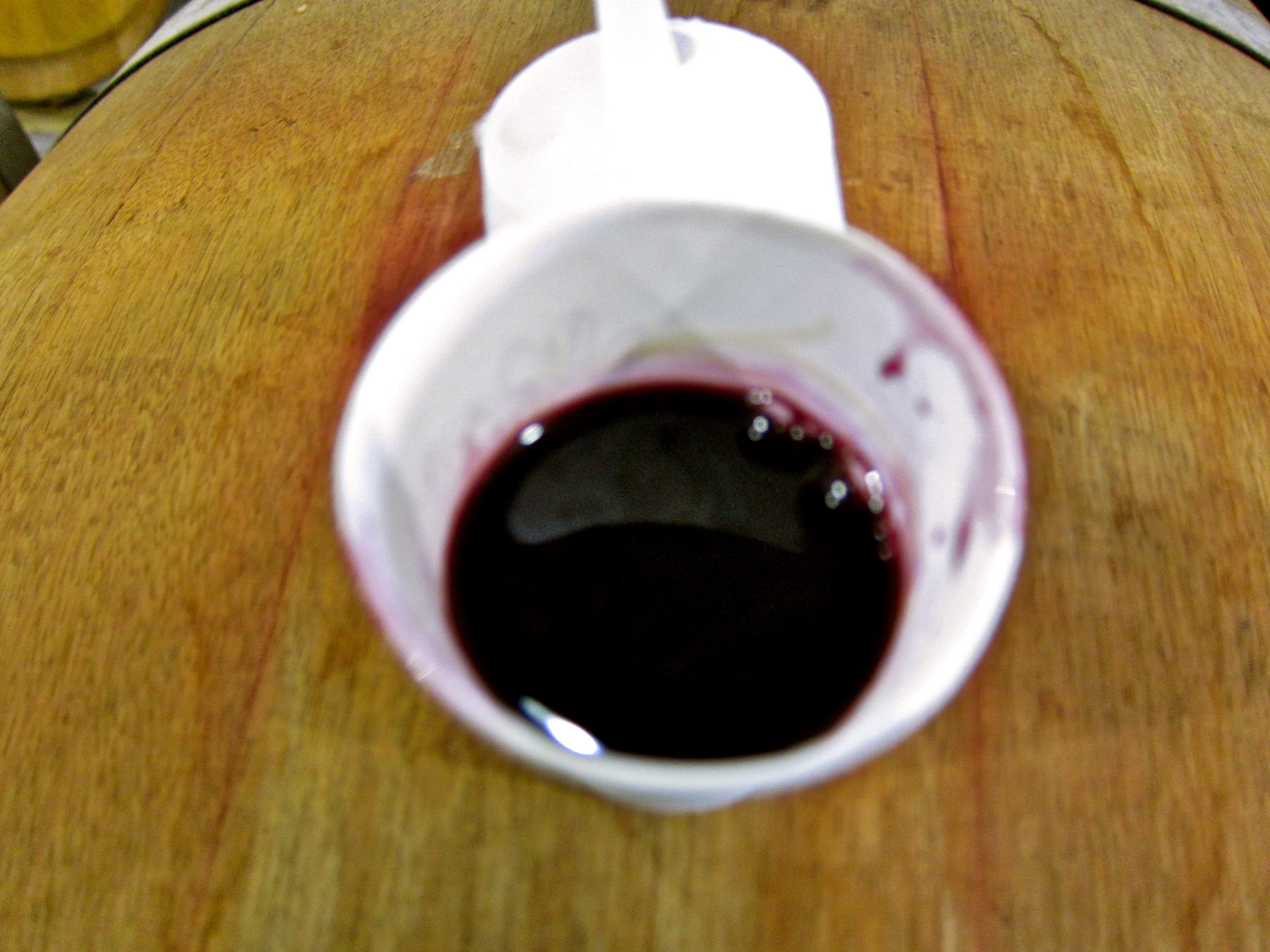 Close-up of a white ceramic cup filled with red wine on a wooden table.