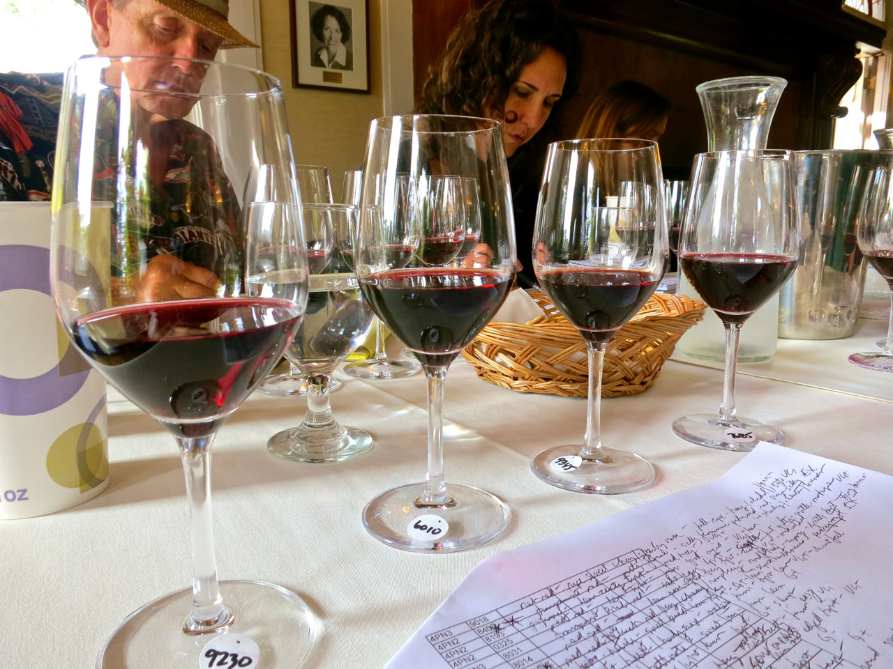 Wine tasting event with multiple glasses of red wine and participants evaluating flavors.