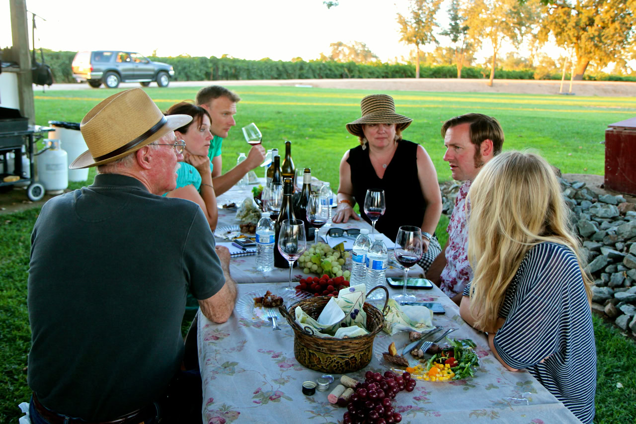 Group enjoying a vineyard dinner with wine and grapes at sunset in Lodi, California.