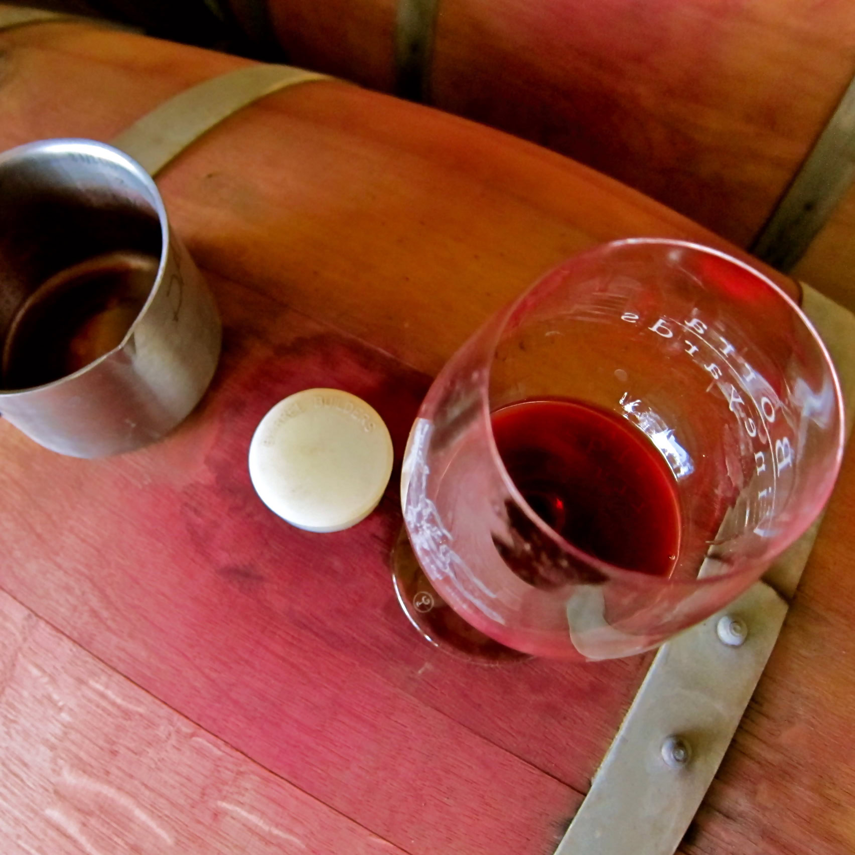 Glass of red wine, metal cup, and cork on a wooden table at Lodi Winegrape Commission.