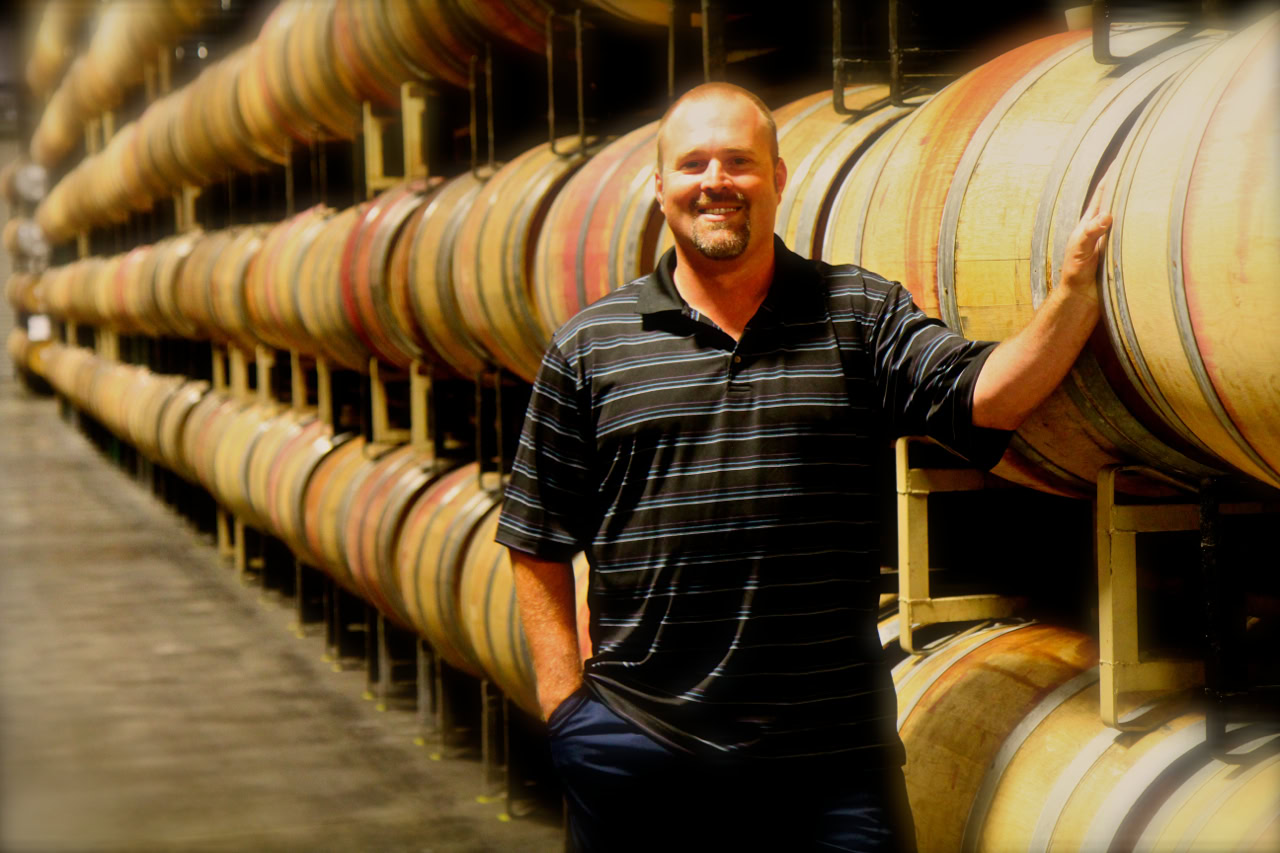 Man smiling at winery with stacked wine barrels in Lodi, California.