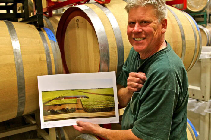 Man holding a wine grape vineyard plan in a winery with wine barrels in the background.