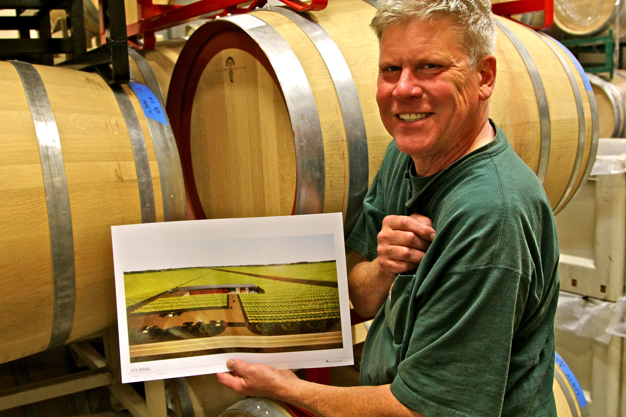 Man holding a wine grape vineyard plan in a winery with wine barrels in the background.