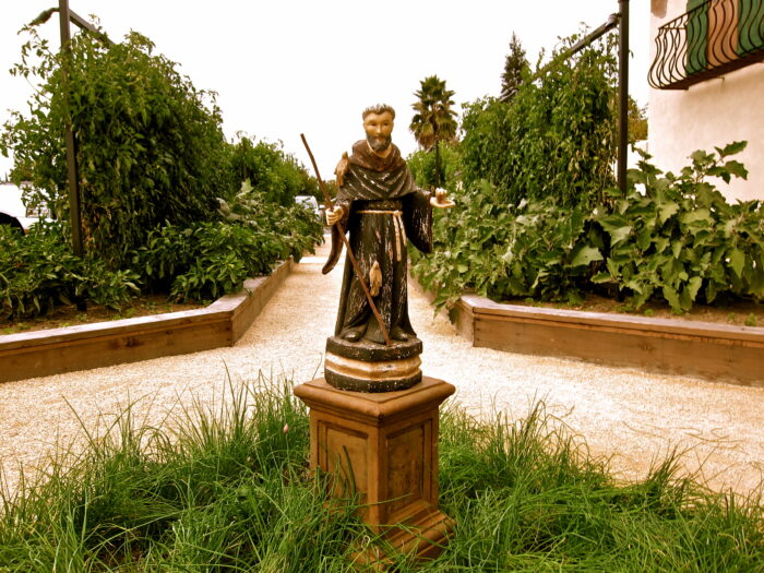 Statue of a monk holding a wine glass in a lush vineyard at Lodi Winegrape Commission.