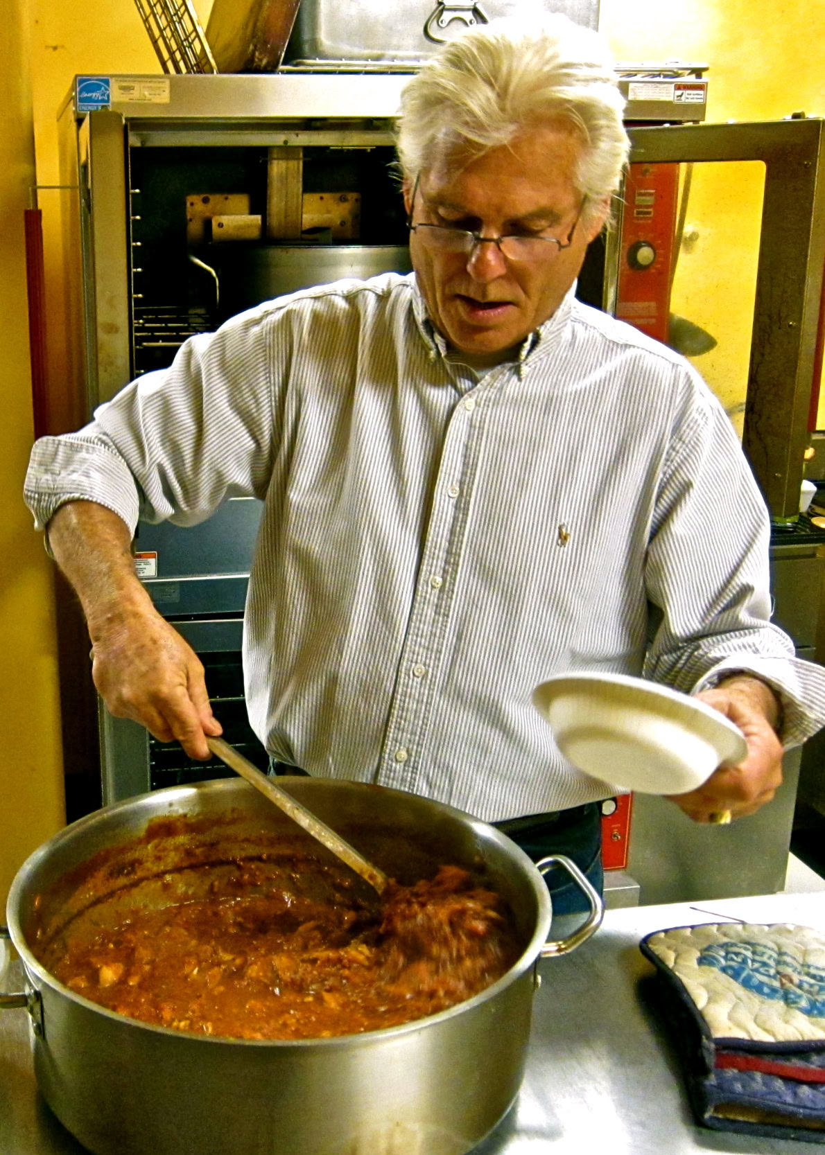 Man cooking stew in a large pot in a kitchen setting, focusing on preparing a hearty meal.