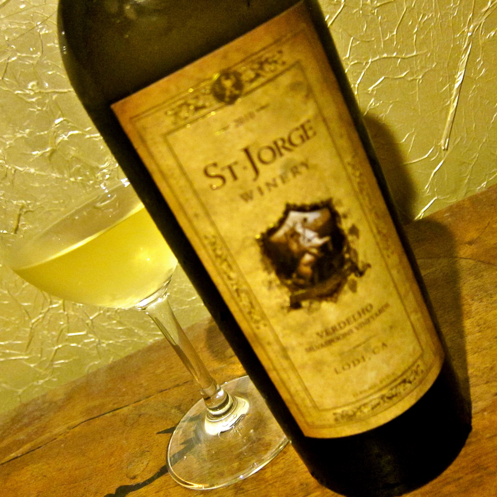 Bottle of St. Jorge Winery Verdelho wine with a glass of white wine on a wooden surface.