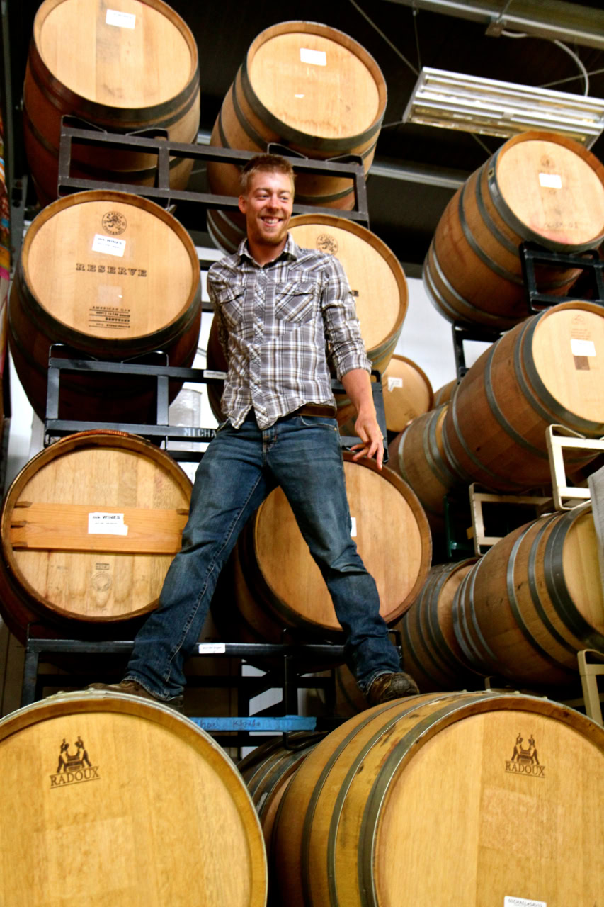 Man standing among stacked wine barrels at Lodi Winegrape Commission facility.