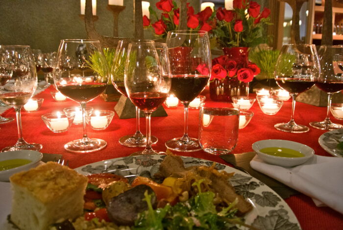 Wine glasses with red wine and a dinner table with food and flowers, representing Lodi Winegrape Commission.